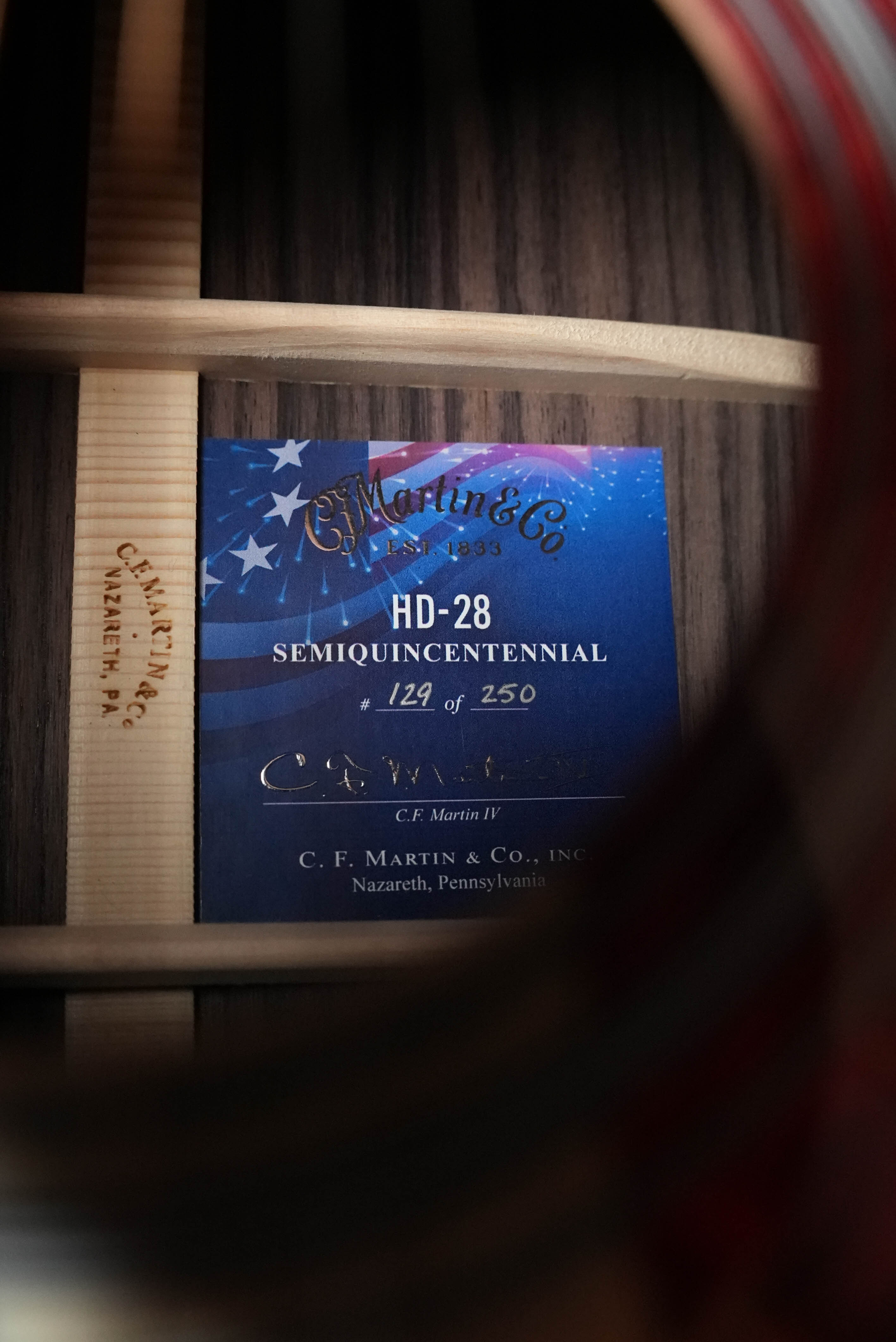 Close-up through guitar strings reveals a Martin & Co. HD-28 Semiquincentennial Limited Edition Custom Ink Design Acoustic Guitar #7873 label with an American flag graphic inside.
