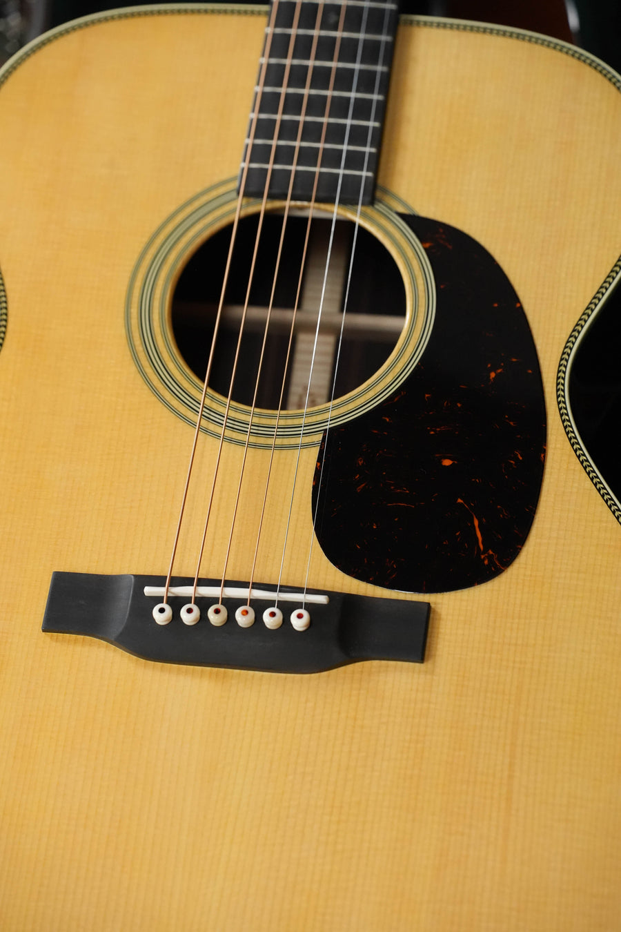 Close-up of the Martin & Co. OOO-28 Gloss Spruce/Rosewood Acoustic Guitar, highlighting its strings, sound hole with decorative edge, dark pickguard, bridge, and light wood body accented by elegant East Indian rosewood.