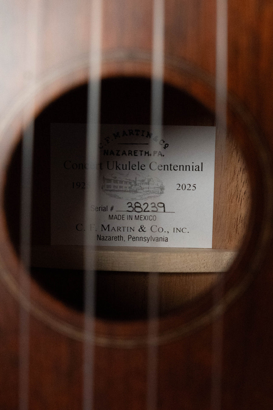 A close-up through the soundhole of a Martin & Co. Centennial Concert All Mahogany Ukulele #8239 shows the label inside reading "Concert Ukulele Centennial 1925-2025," made by Martin & Co.