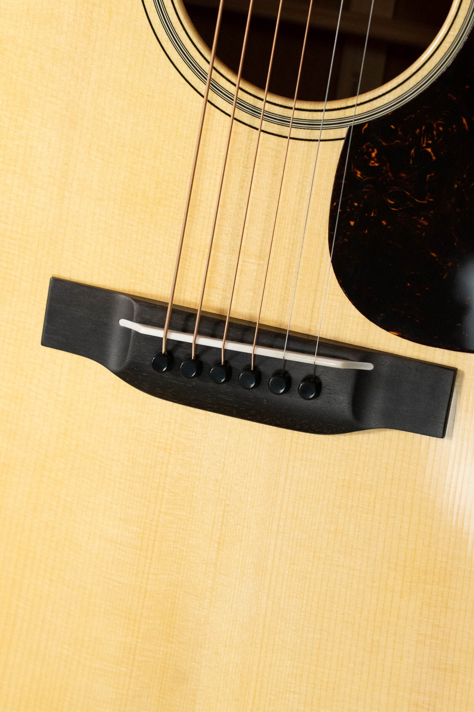 Close-up of a Martin & Co. Custom Shop D-18V Adirondack/Mahogany Dreadnought Acoustic Guitar #6905, highlighting its light Adirondack spruce top, bridge, saddle, six strings, and black pickguard.