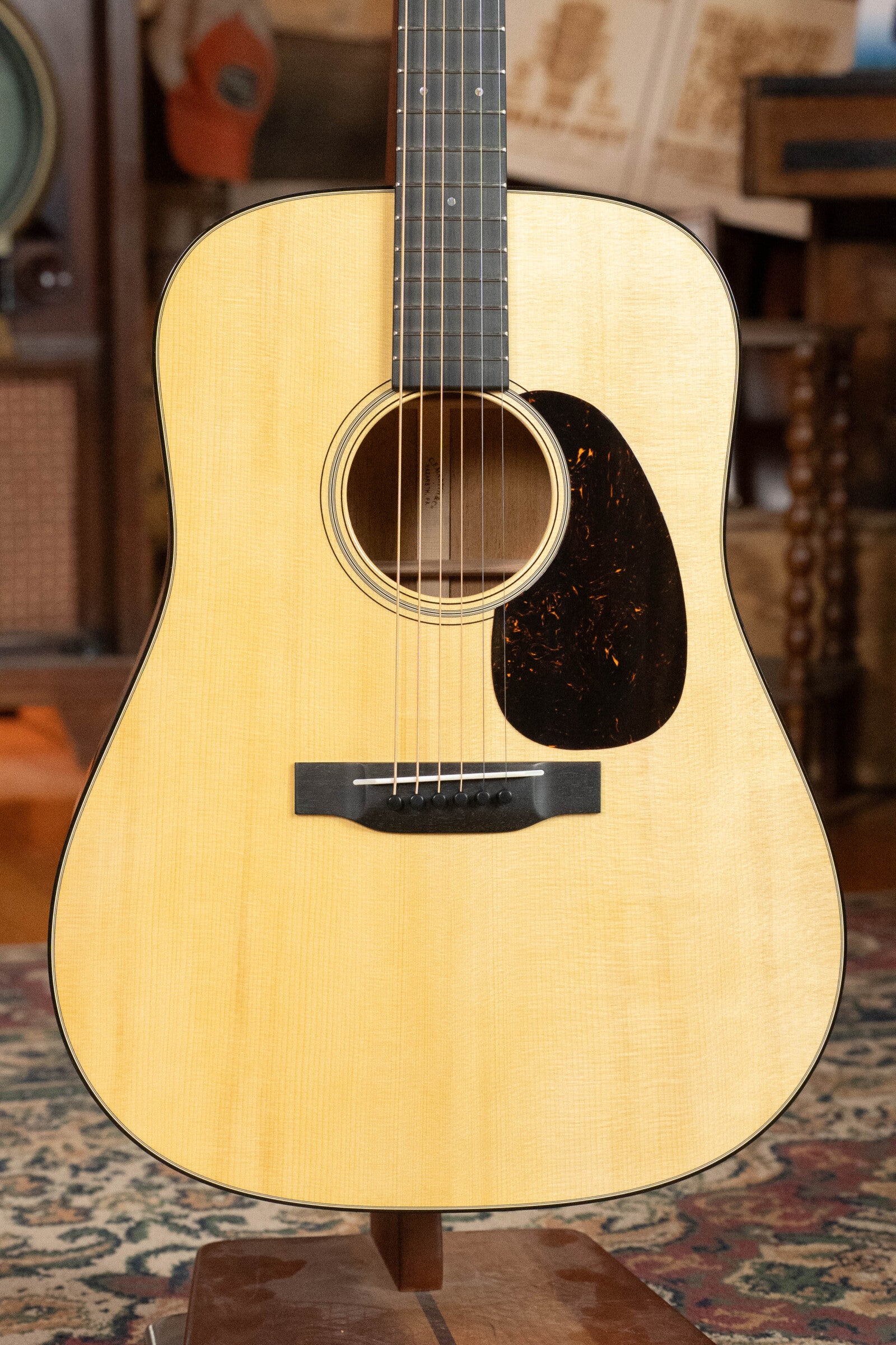 A Martin & Co. Custom Shop D-18V Adirondack/Mahogany Dreadnought Acoustic Guitar #6905 stands upright in a cozy, vintage-themed room with a patterned rug, featuring a black pickguard and dark fretboard.