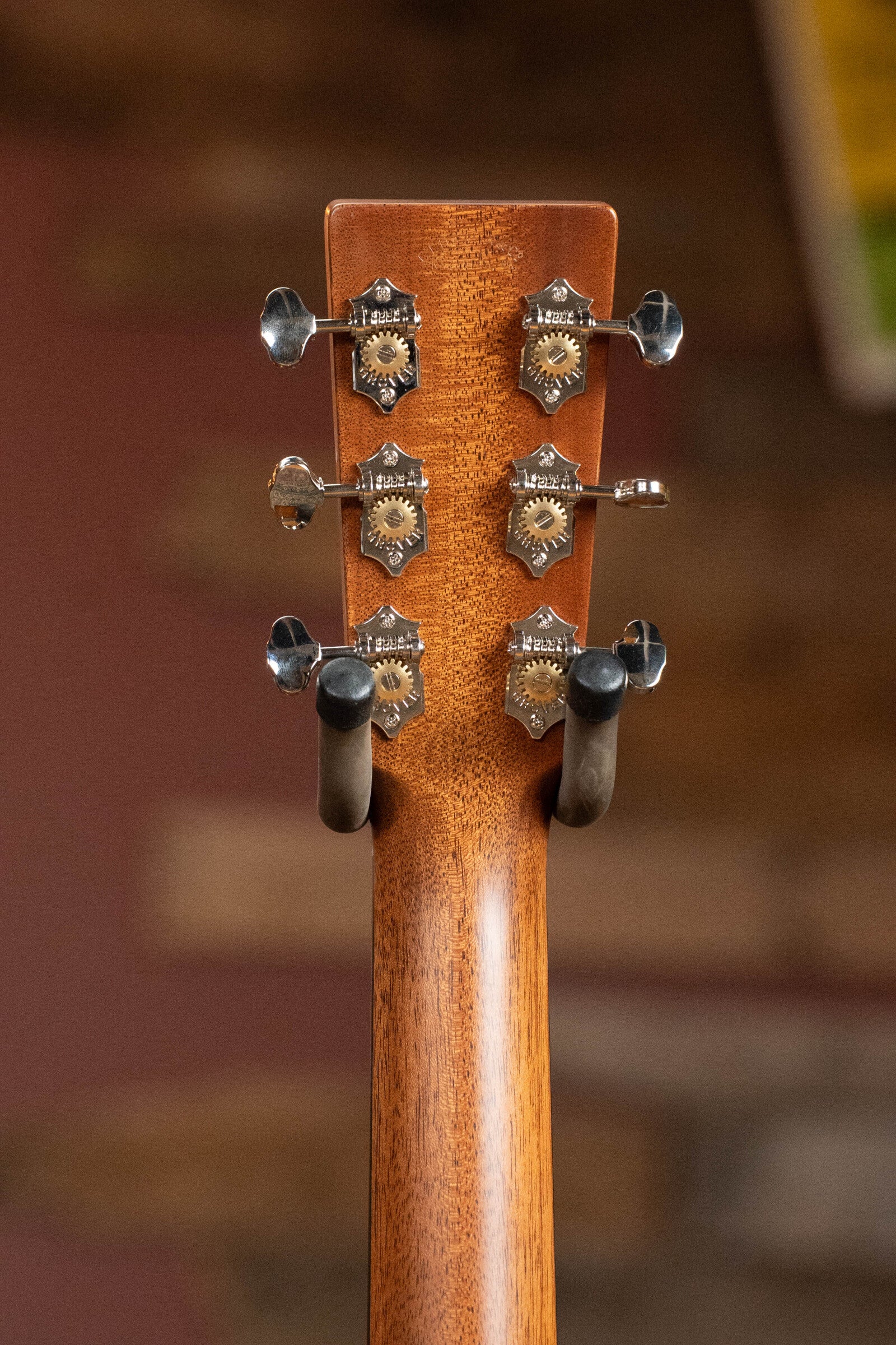 Close-up of the Martin & Co. Custom Shop D-18V Adirondack/Mahogany Dreadnought Acoustic Guitar #6905 headstock, featuring six silver tuning pegs and visible wood grain, with a blurred background and mounted on a stand.