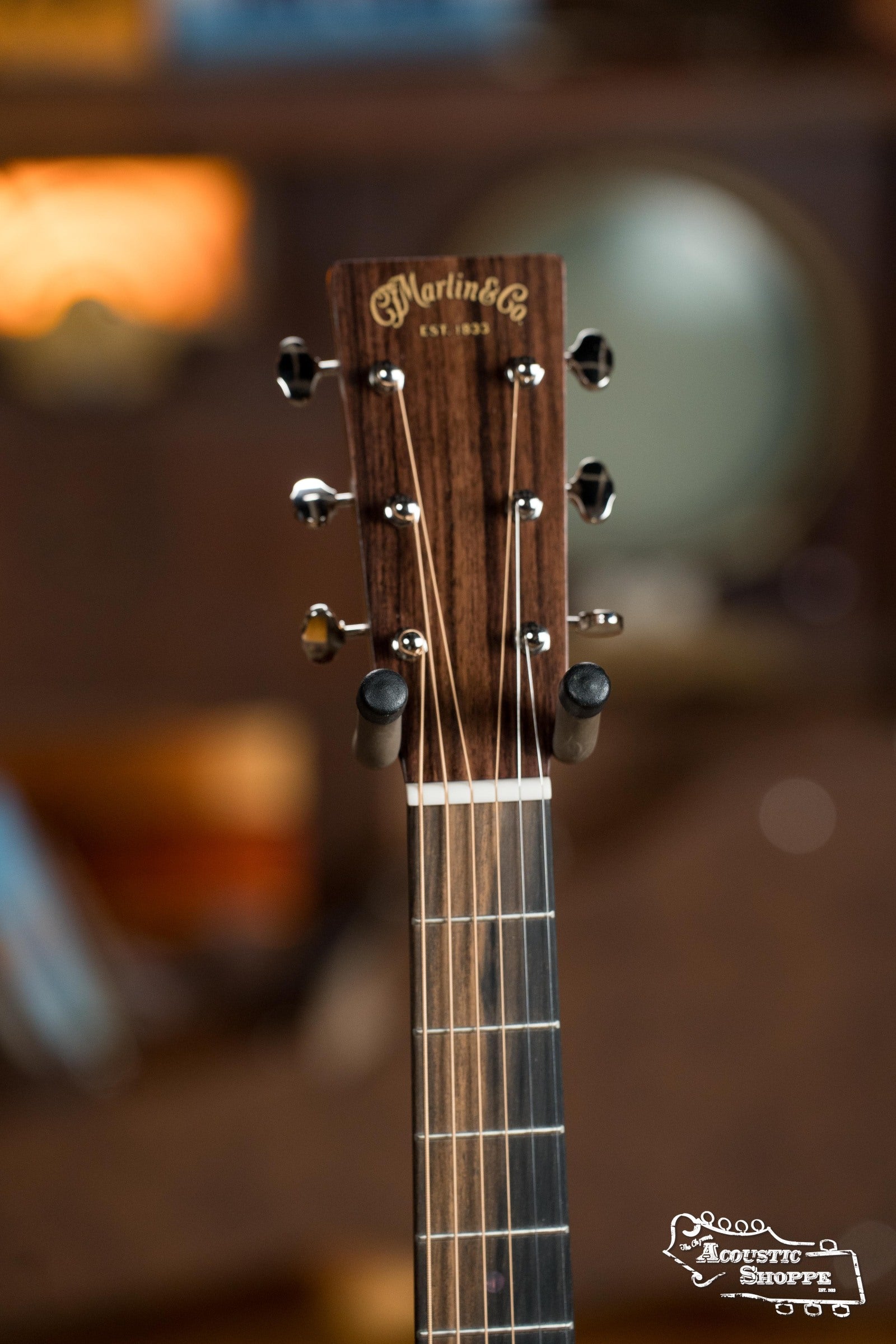 Close-up of the Martin & Co. DE Retro Plus Torrefied Spruce/Mahogany Dreadnought Guitar headstock, showing tuning pegs and logo with blurred background and Acoustic Shoppe watermark, highlighting its vintage-inspired tone.