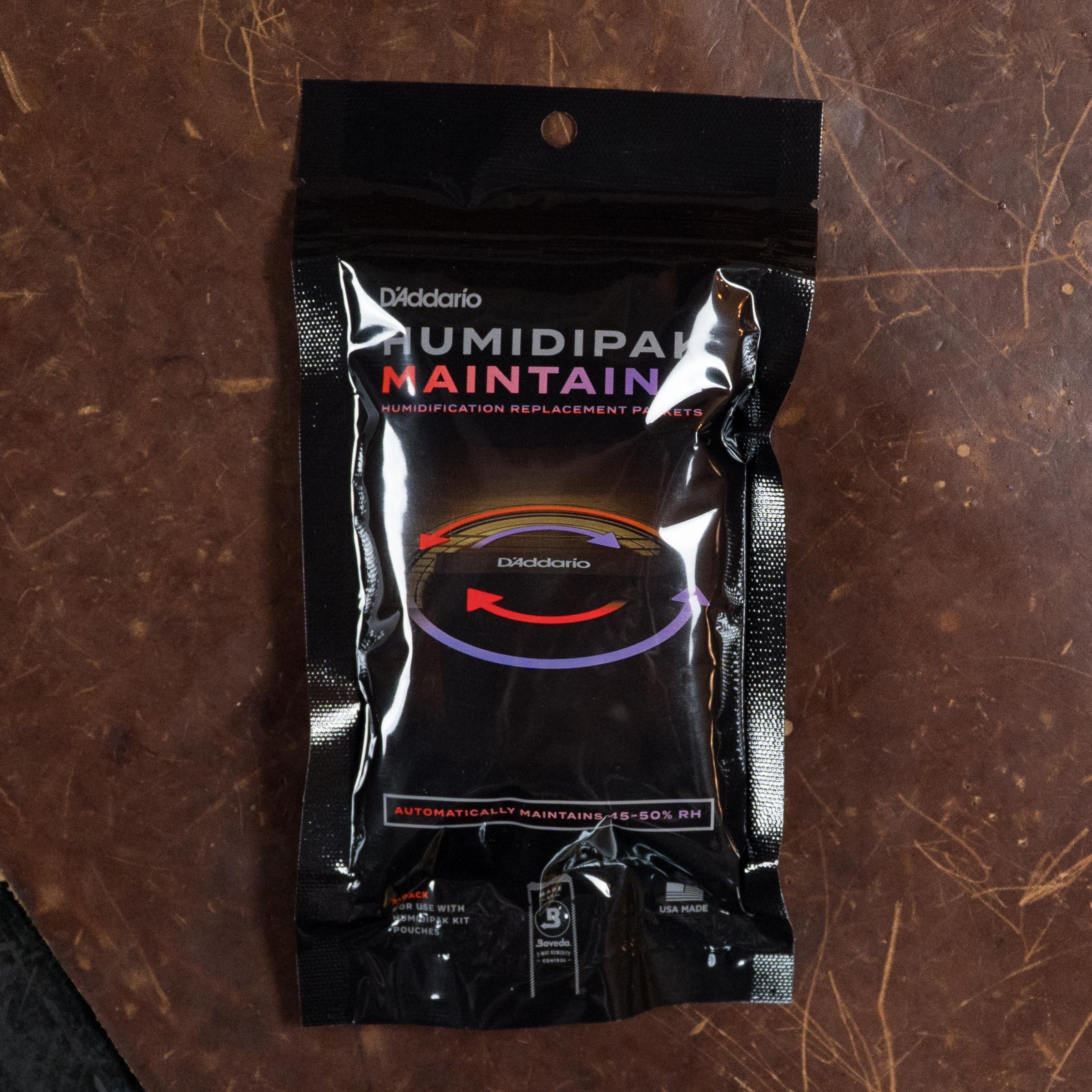 A black, resealable pack of D’Addario Humidipak Maintain sits on a brown surface—ideal for keeping your Martin & Co. DE Retro Plus Torrefied Spruce/Mahogany Dreadnought Guitar at 45-50% RH to preserve its vintage-inspired tone.