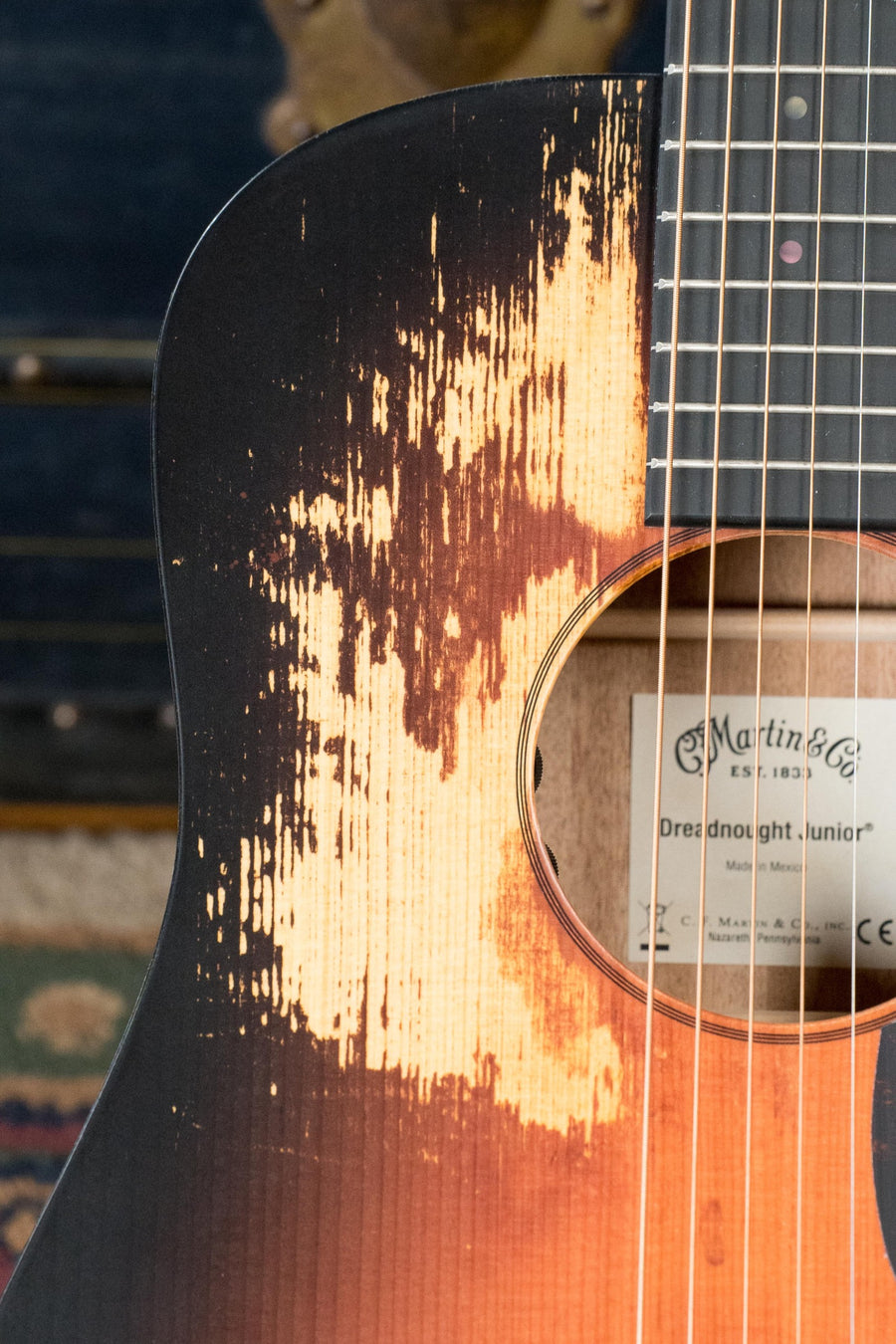 A close-up of the *New 2025 Model* Martin D Jr E Streetlegend Burst Spruce/Sapele Aged-Look Dreadnought Guitar (#3849) by Martin & Co. shows distressed wood on the body and the label inside, highlighting its vintage-inspired design and modern electronics.