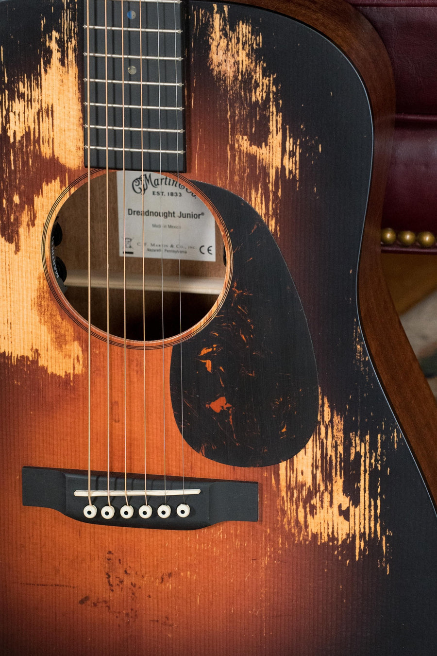A close-up shows a *New 2025 Model* Martin & Co. D Jr E Streetlegend Burst Spruce/Sapele Aged-Look Dreadnought Guitar (#3865) with scratches, six strings, the sound hole, and a label reading "Dreadnought Junior" inside.