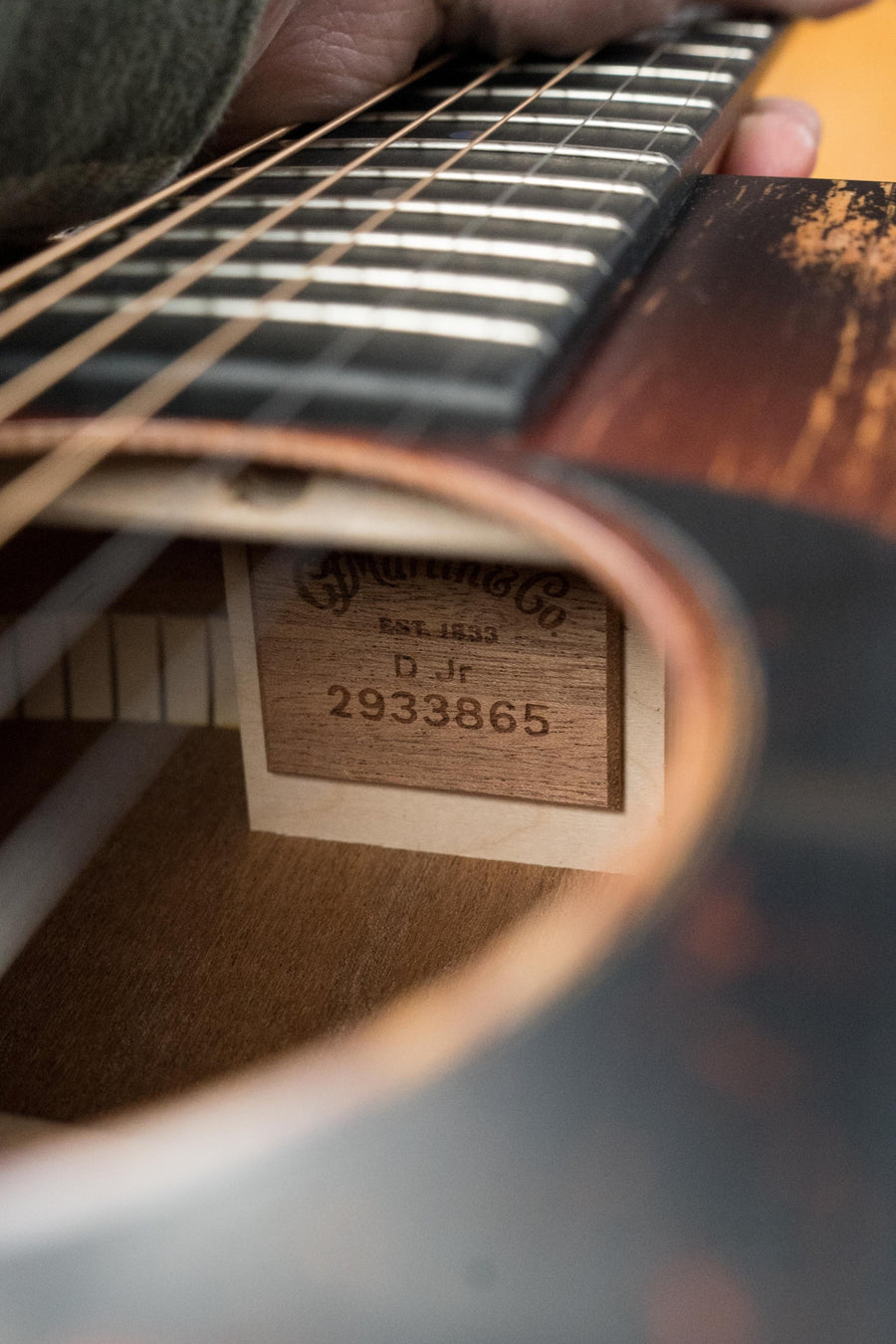 Close-up of a hand holding the neck of the *New 2025 Model* Martin D Jr E Streetlegend Burst from Martin & Co., showing its inside label and serial #3865 through the soundhole of this aged-look spruce/sapele dreadnought with built-in electronics.