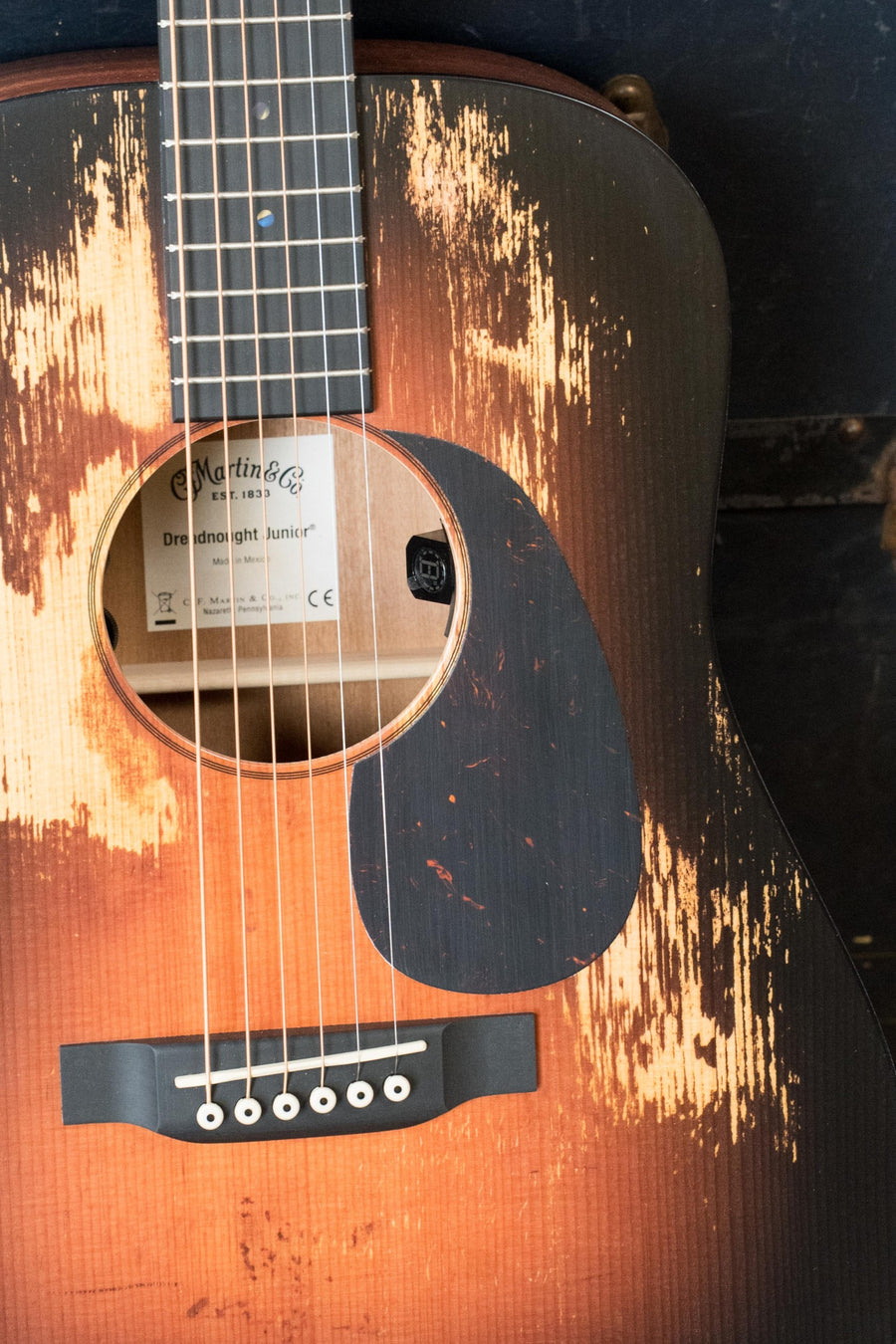 A close-up of the *New 2025 Model* Martin & Co. D Jr E Streetlegend Burst Spruce/Sapele Aged-Look Dreadnought Guitar #3866, highlighting its distressed finish, strings, sound hole, and bridge. Features Martin electronics.