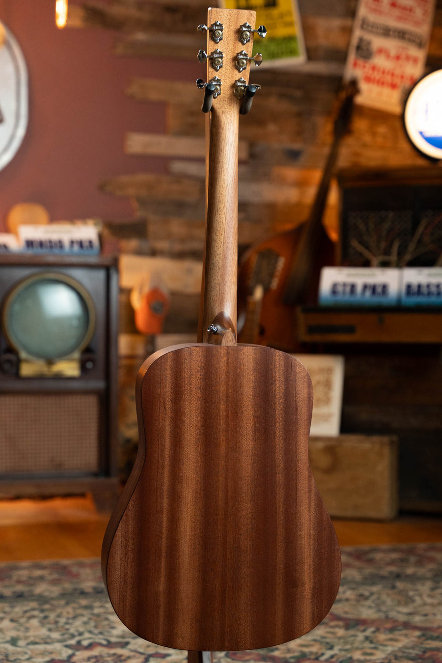 The Martin & Co. D Jr E Streetlegend Burst Spruce/Sapele Aged-Look Dreadnought Guitar (#3872) is displayed from the back on a patterned rug in a cozy, vintage-inspired room with retro decor and music-themed wall art.