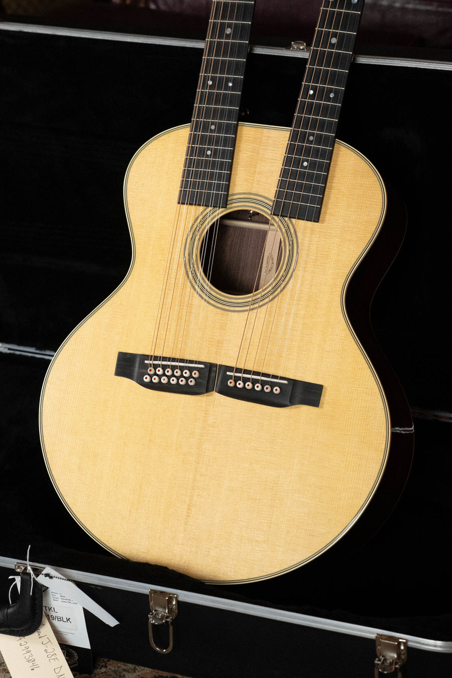 A Martin & Co. Grand J-28E DN Spruce/Rosewood Double Neck Jumbo Guitar w/Fishman Pickup (#3046), featuring 12 and 6-string necks and a light top with dark sides, is displayed in an open black case, tags attached.