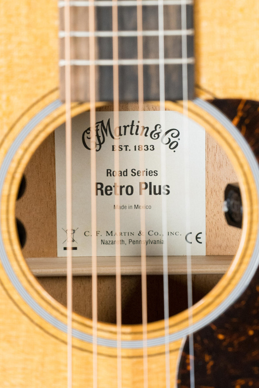 Close-up of a *New 2025 Model* Martin & Co. OOOE Retro Plus Torrefied Spruce/Mahogany OOO Guitar’s sound hole, highlighting the label with model details and Martin Electronics #8194 inside.