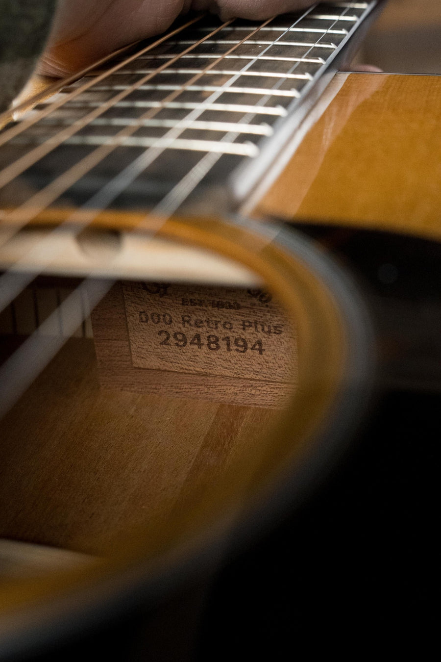 Close-up through the soundhole of a Martin & Co. *New 2025 Model* OOOE Retro Plus Guitar, serial #8194, showing a hand pressing strings and highlighting its torrefied spruce top and mahogany body with Martin Electronics.