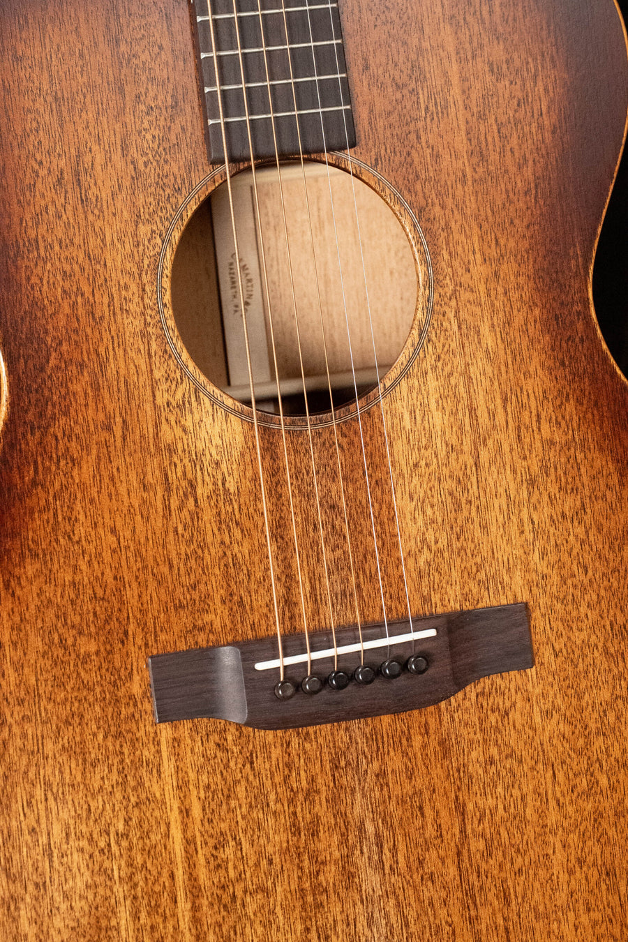Close-up of the Martin & Co. OOO-15M StreetMaster All Mahogany Acoustic Guitar #4910, showing its wooden soundboard, round soundhole, six strings, dark bridge with black pins, and the distinctive natural grain and vintage craftsmanship.