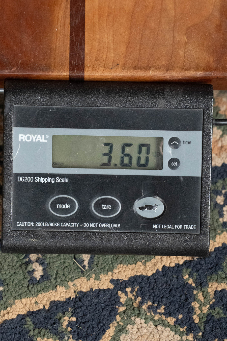 A digital shipping scale reads 3.60 pounds atop a patterned carpet and wood, invoking the craftsmanship of the Martin & Co. OOO-15M StreetMaster All Mahogany OOO Acoustic Guitar #4910.