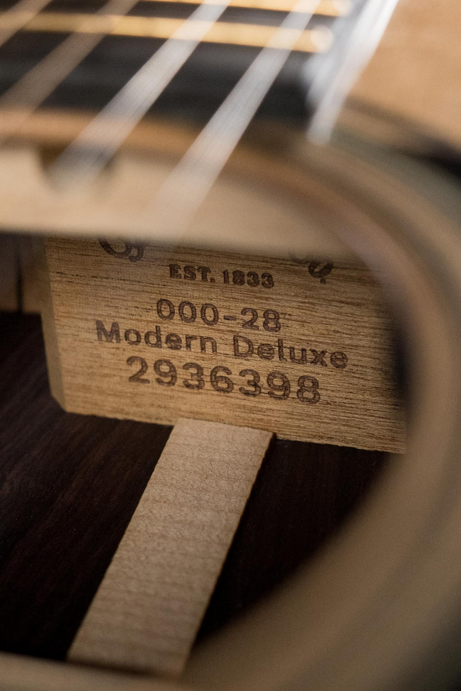 Close-up through the soundhole of a Martin & Co. OOO-28E Modern Deluxe Spruce/Indian Rosewood Guitar w/Electronics #6398, showing its interior label. The solid spruce top and vintage-style strings are partially visible above.