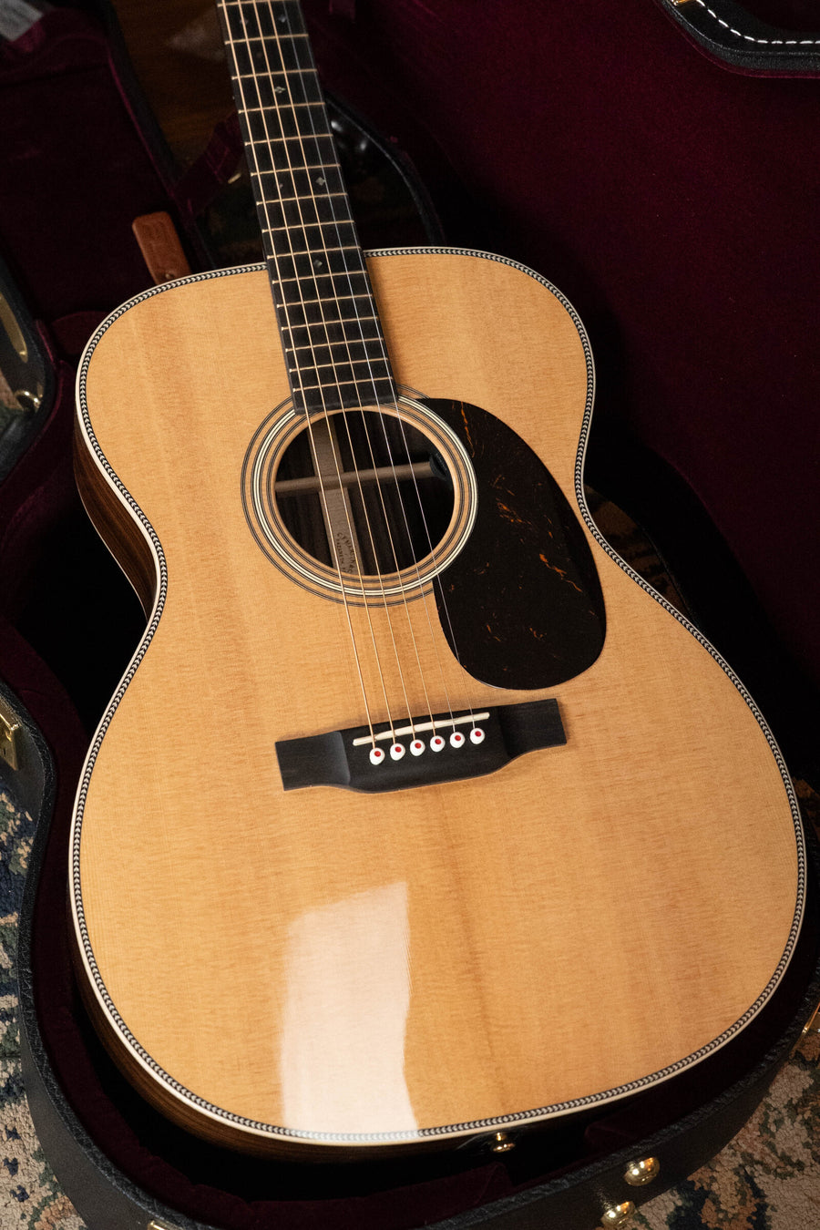 A Martin & Co. OOO-28E Modern Deluxe Spruce/Indian Rosewood Guitar w/Electronics #9400 rests in a plush-lined case, showing its solid spruce top, dark pickguard, decorative binding, visible strings, frets, and sound hole.