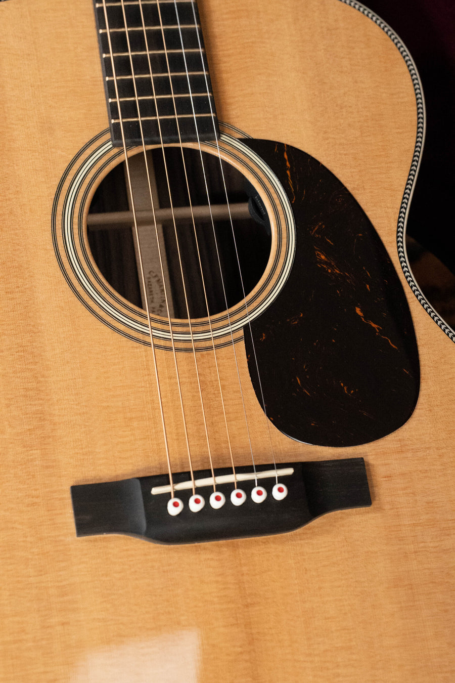 Close-up of a Martin & Co. OOO-28E Modern Deluxe Spruce/Indian Rosewood Guitar w/Electronics #9400, highlighting its sound hole, pickguard, bridge, and fretboard—solid spruce top resting on a wooden surface.