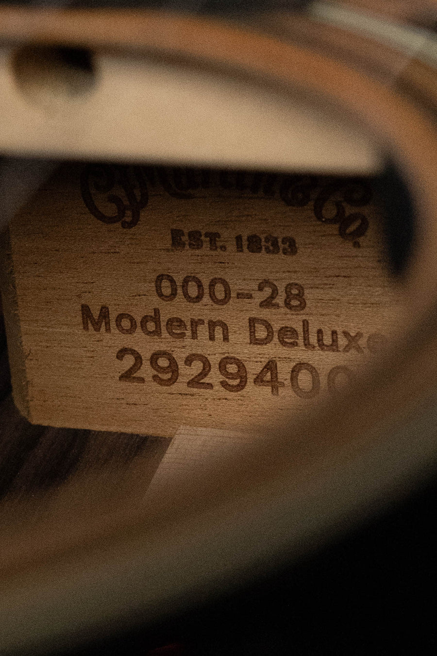 Close-up view inside a vintage-style Martin & Co. OOO-28E Modern Deluxe Spruce/Indian Rosewood Guitar w/Electronics #9400, showing a wooden label with “Est. 1833” and model details on the solid spruce top.