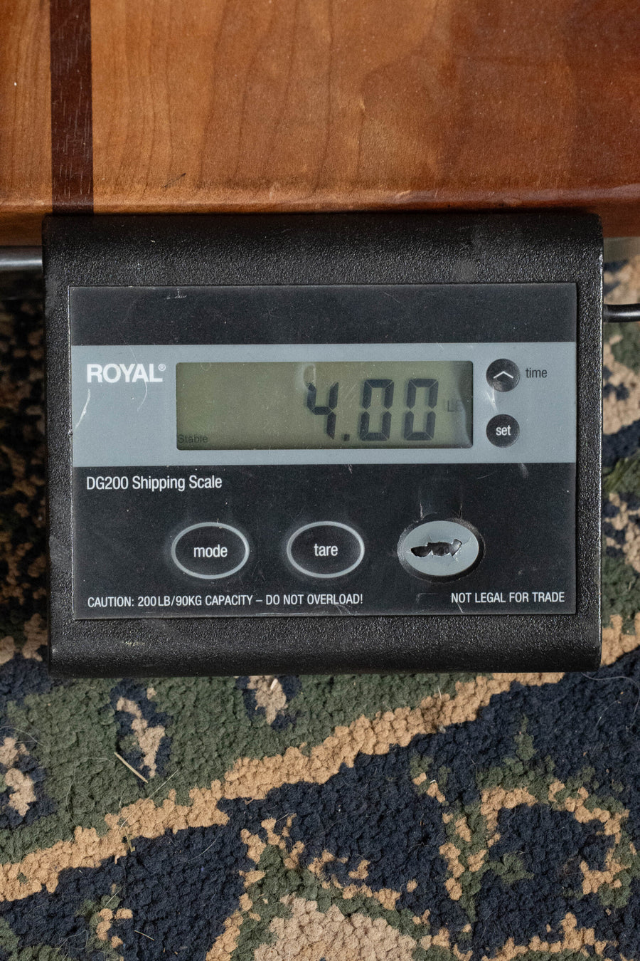 A digital shipping scale on patterned carpet shows 4.00 lbs—ideal for weighing a vintage-inspired Martin & Co. OOO-28E Modern Deluxe Spruce/Indian Rosewood OOO Guitar w/Electronics #9400. The ROYAL DG200 Scale includes buttons and an overload warning.