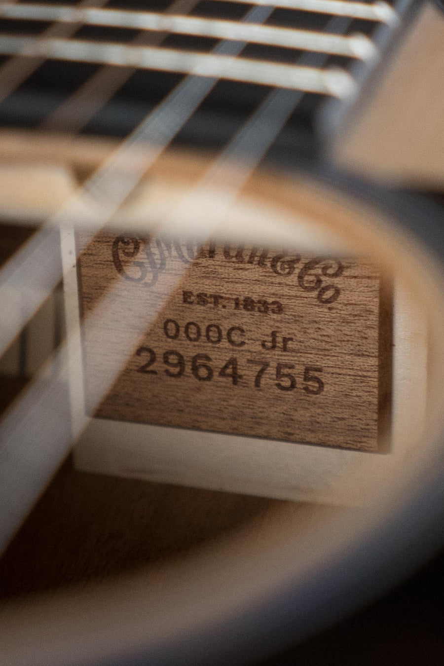Close-up of a Martin & Co. OOO Jr CE Spruce/Sapele Cutaway Guitar (#4755), showing the wooden label through strings and soundhole of the acoustic-electric body with built-in Martin electronics.