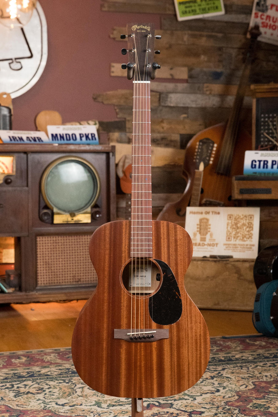Martin OOO Jr E acoustic guitar with all-sapele body, black pickguard, and natural finish standing on a patterned rug. - Martin OOO Jr E All Sapele OOO Guitar w/Martin Electronics #4824 - Default Title