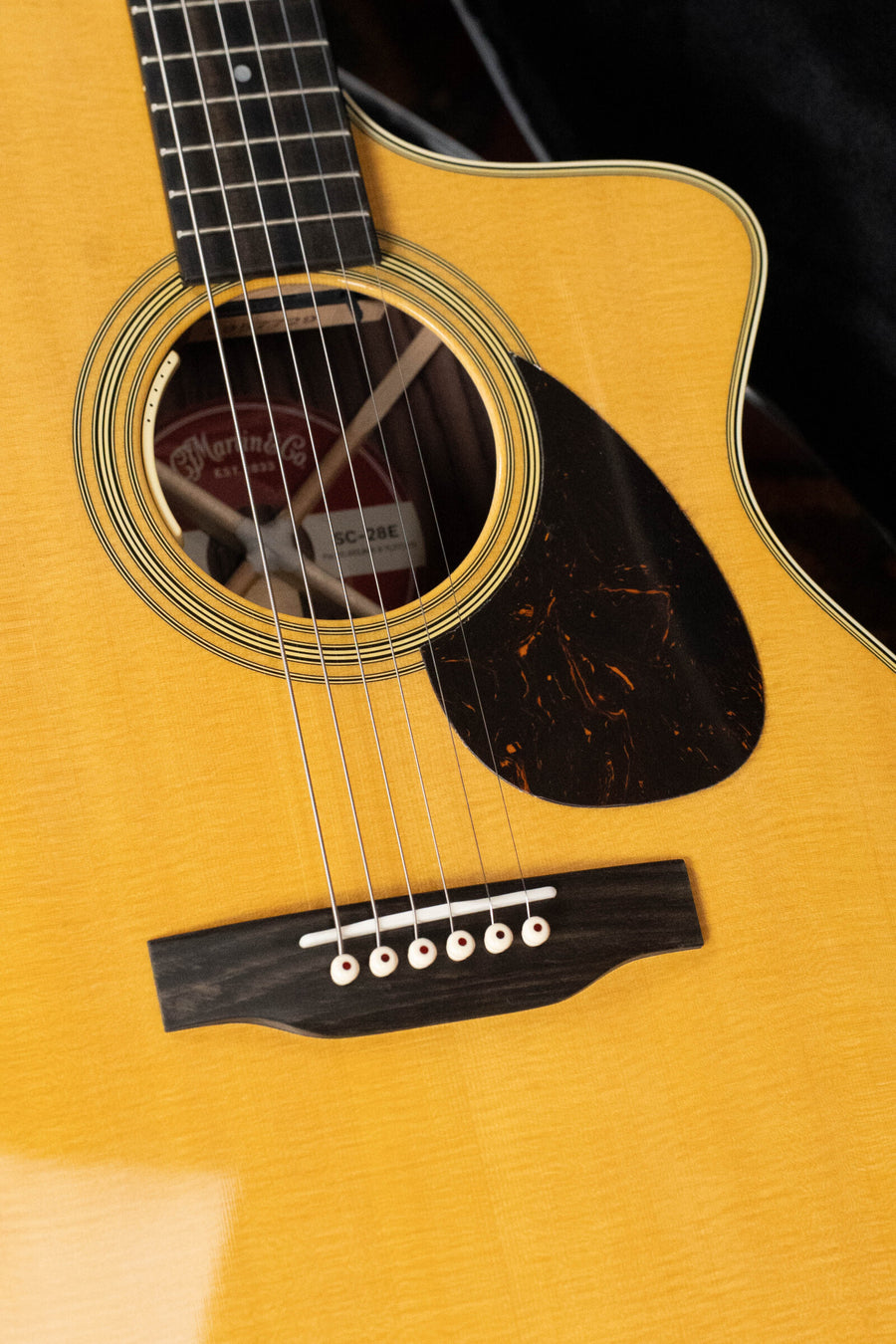 Close-up of the Martin & Co. SC-28E Spruce/Indian Rosewood S Body Cutaway Guitar w/Fishman Electronics, showing its strings, bridge, glossy Indian rosewood body, and visible Martin & Co. label inside the soundhole.
