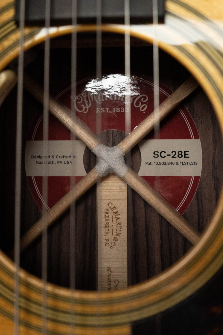 Close-up view through the strings of a Martin & Co. SC-28E Spruce/Indian Rosewood S Body Cutaway Guitar w/Fishman Electronics, focusing on the interior label marked Martin & Co. and Crafted in Nazareth, PA USA.