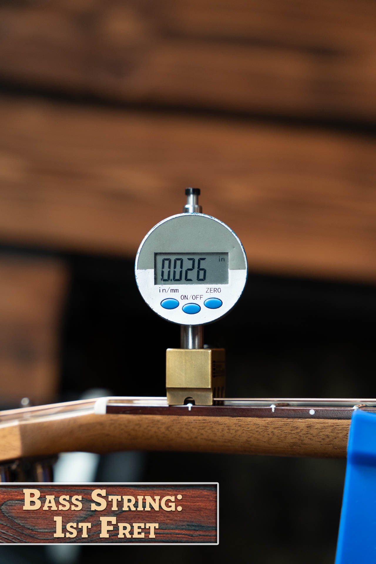 A digital gauge reads 0.026 inches above the first fret of a Maton T.E. Personal Spruce/Queensland Maple Deep Body OO Guitar w/Electronics #0085 by Maton Guitars. The label below says Bass String: 1st Fret; background is blurred wood.