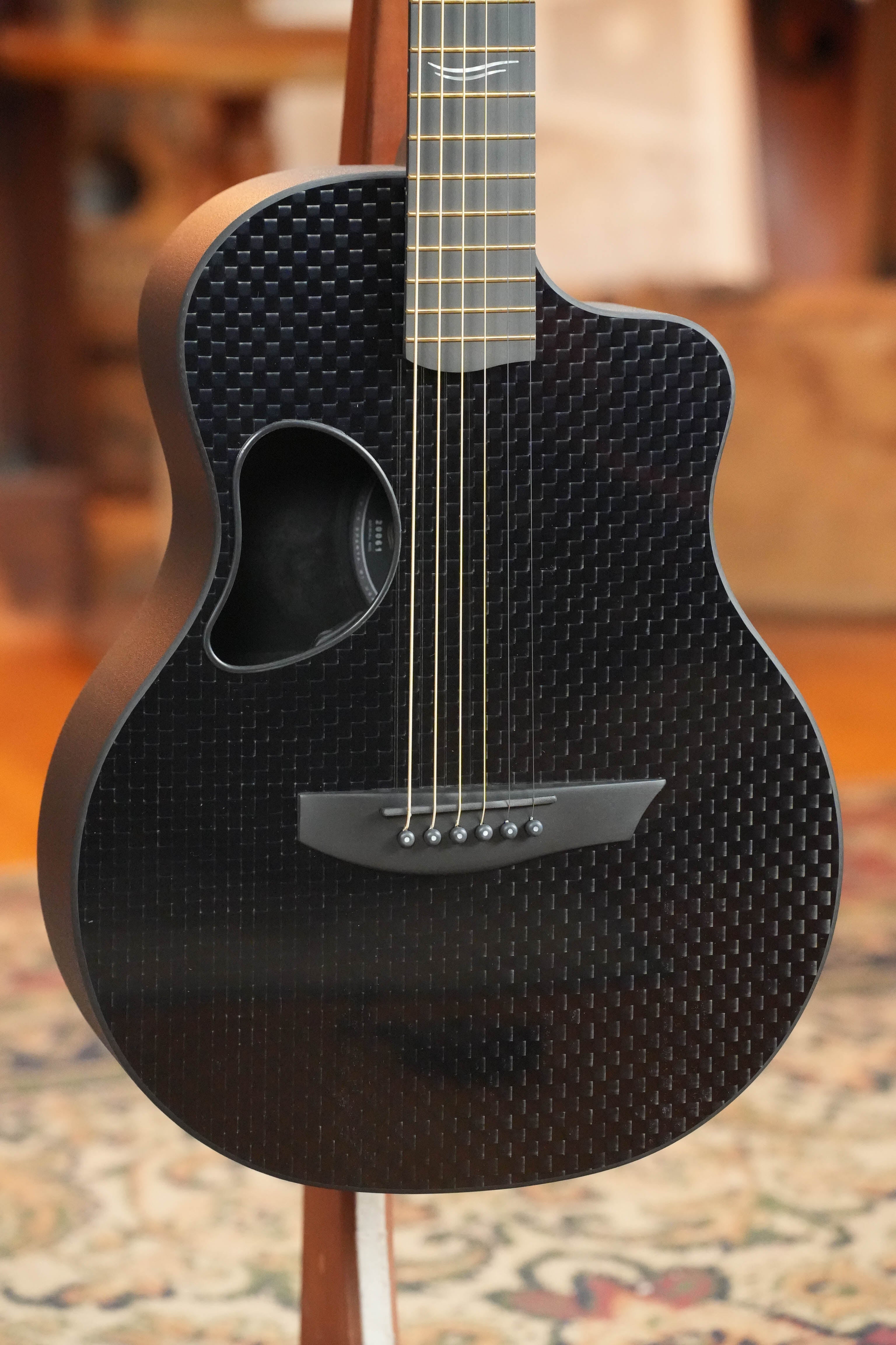A close-up of the McPherson Guitars Carbon Fiber Touring Series Blackout Basketweave Guitar w/L.R. Baggs Element Pickup #0061, featuring a modern bridge, unique soundhole, and premium performance—ideal for touring musicians.