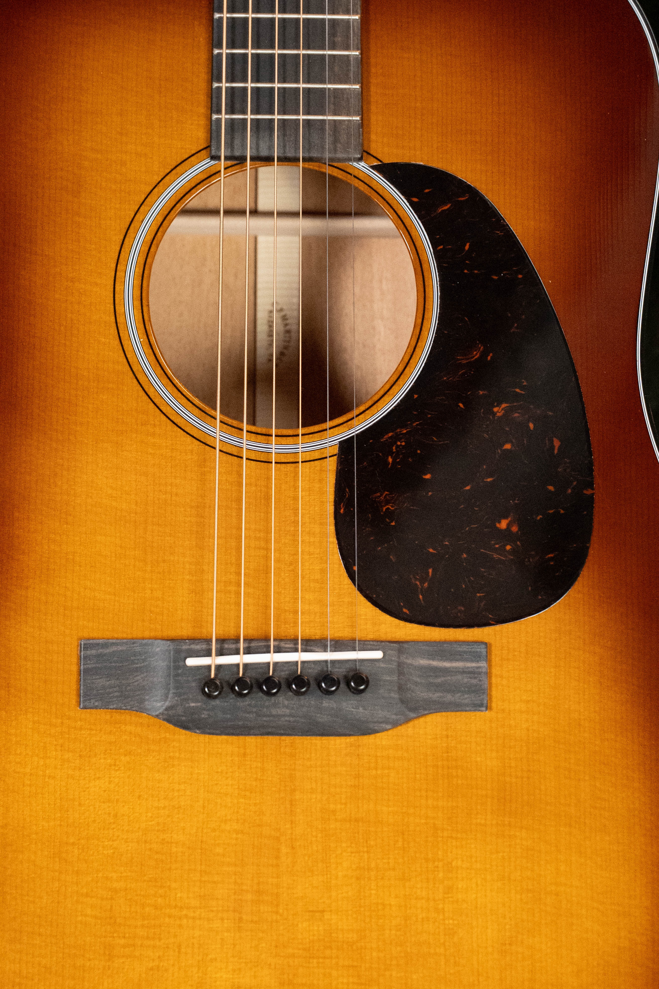 Close-up of the *New 2025 Model* Martin D-18 1933 Gloss Ambertone Spruce/Mahogany Dreadnought by Martin & Co., showcasing its strings, sound hole, pickguard, bridge, warm wood finish, and classic GE-scalloped X-bracing.