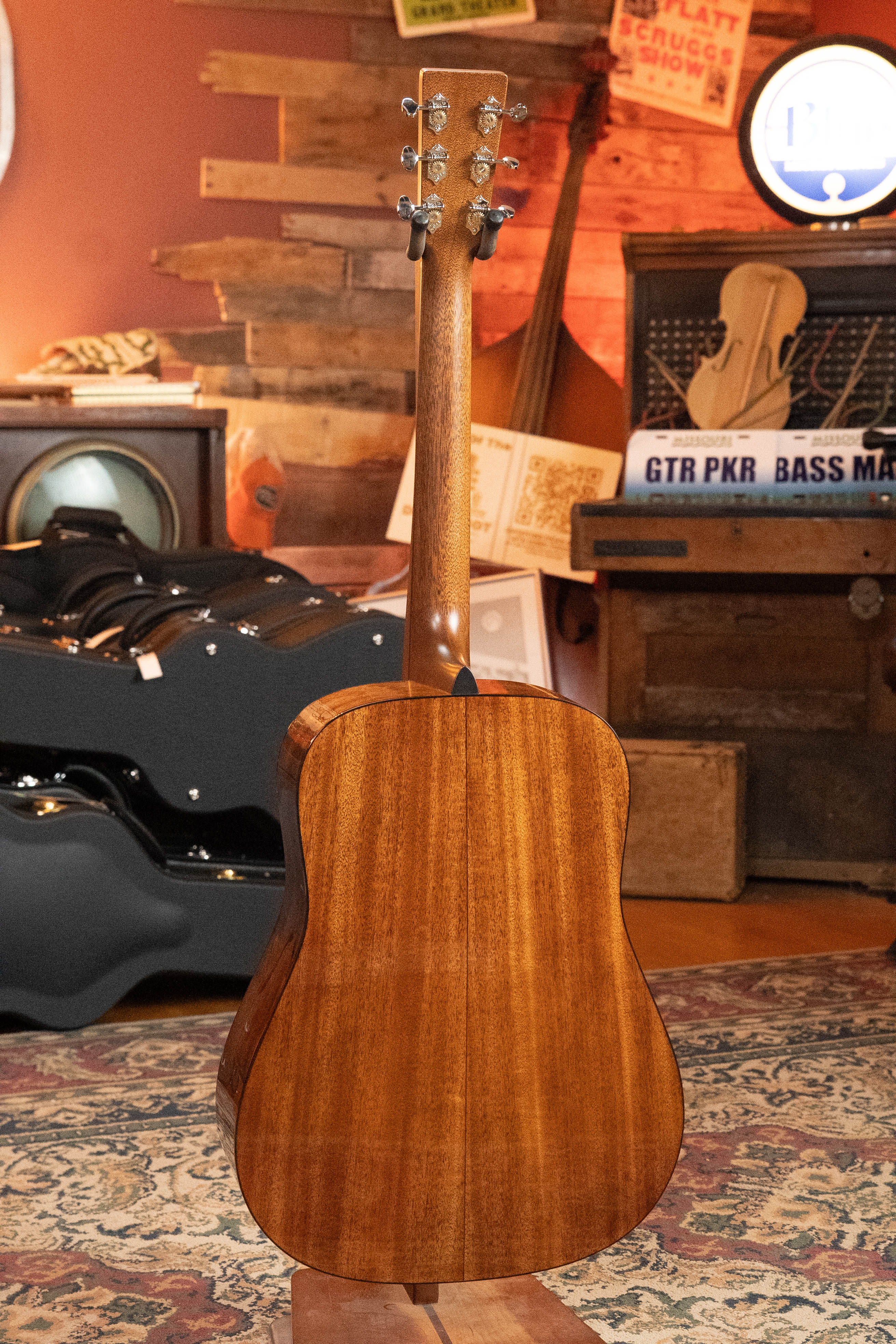 A *New 2025 Model* Martin & Co. D-18 1933 Gloss Ambertone Spruce/Mahogany Dreadnought Acoustic Guitar (#6784) is shown with its back to the camera in a cozy, vintage-inspired room filled with instruments, cases, rugs, and wood paneling.