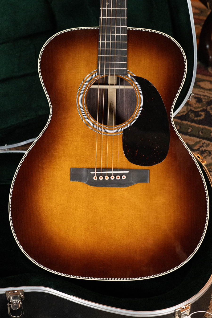 A Martin & Co. OOO-28 Gloss 1933 Ambertone Spruce/Rosewood acoustic guitar (#3434) with six strings and a dark pickguard is displayed resting in an open black case lined with green velvet.