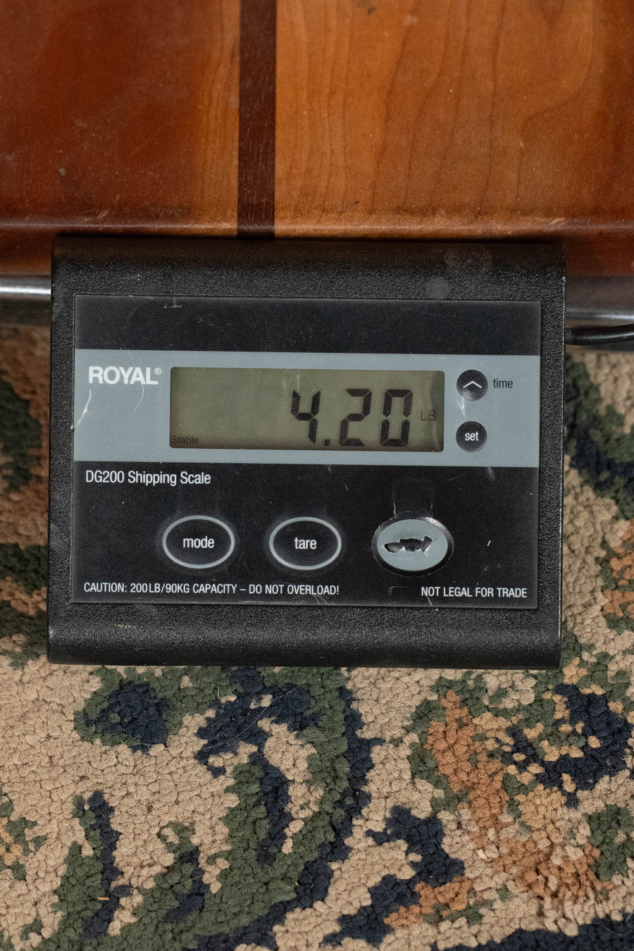 A black digital shipping scale with a Royal logo, placed on a patterned carpet before a wooden surface, displays 4.20 lbs—possibly weighing the Martin & Co. OOO-28 Gloss 1933 Ambertone Spruce/Rosewood Acoustic Guitar #3434.