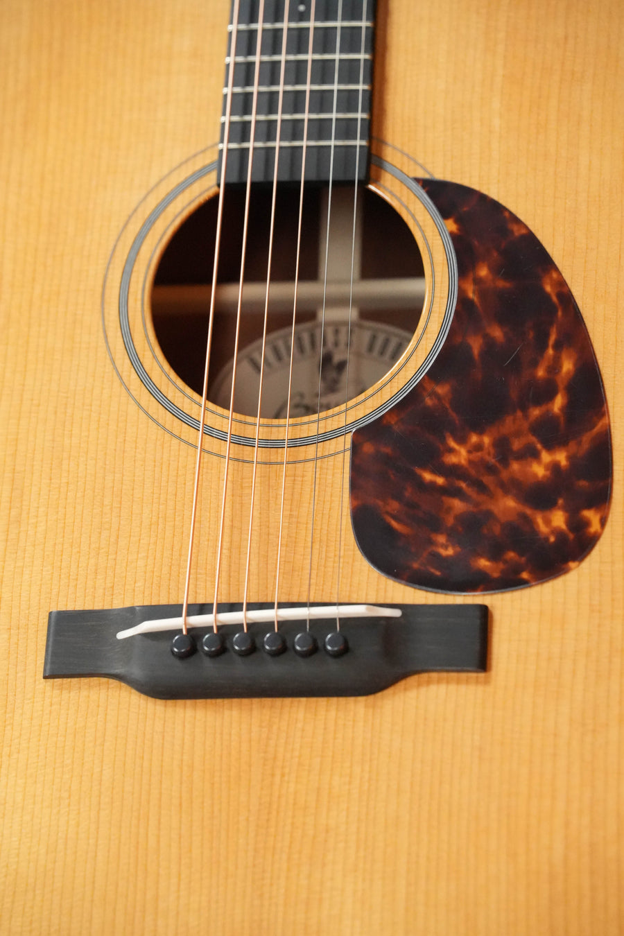Close-up of a Boucher Guitars *New 2026 Model* BG-42T-G Bluegrass Goose Gold Pack dreadnought, highlighting six strings, sound hole, tortoiseshell-patterned pickguard, and part of the bridge on torrefied Adirondack/mahogany body.