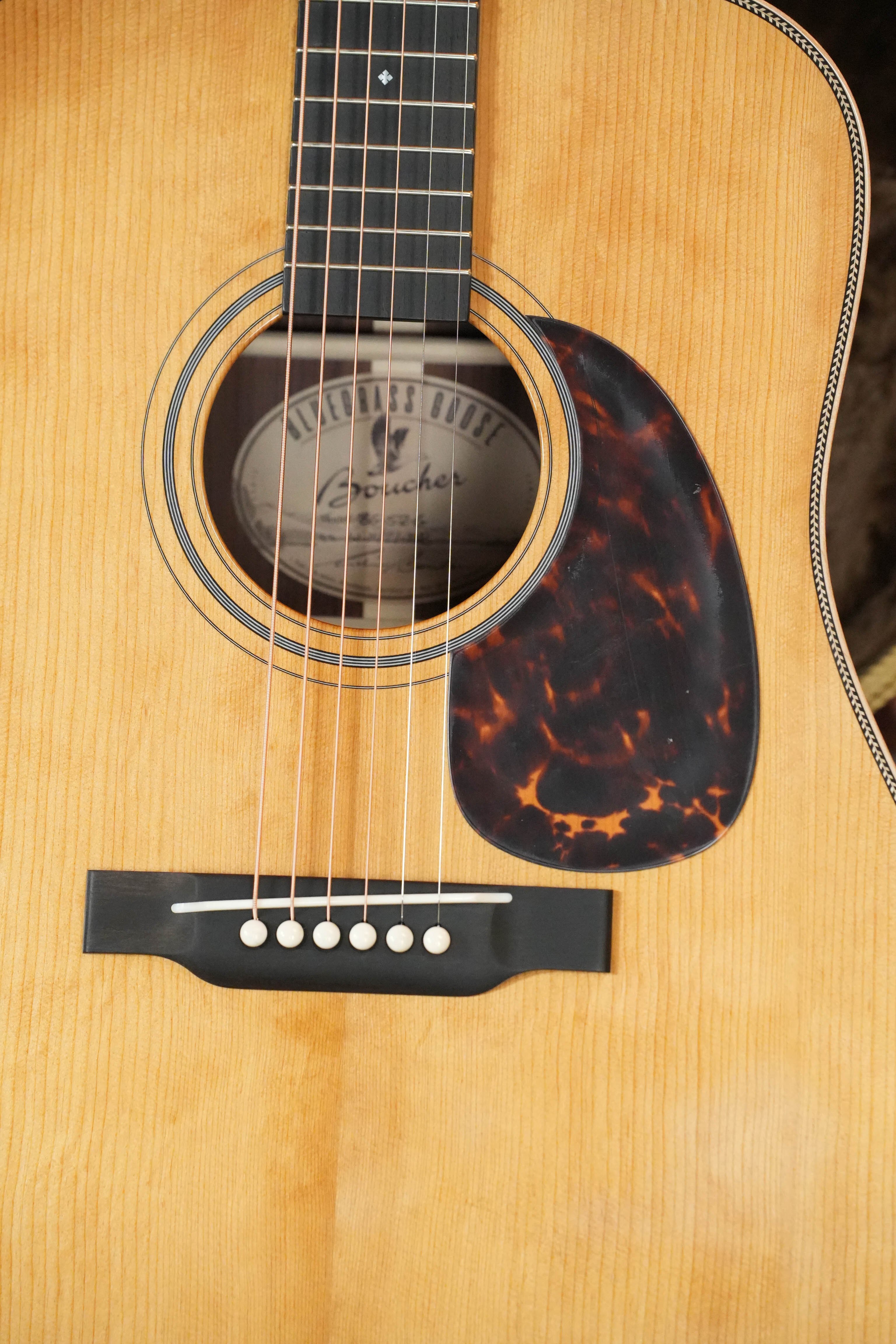 A close-up of the *New 2026 Model* Boucher BG-52-G Torrefied Adirondack/Rosewood Bluegrass Goose Gold Pack Dreadnought Acoustic Guitar #1421 by Boucher Guitars, showing its six strings, sound hole with label, tortoiseshell pickguard, and fretboard.