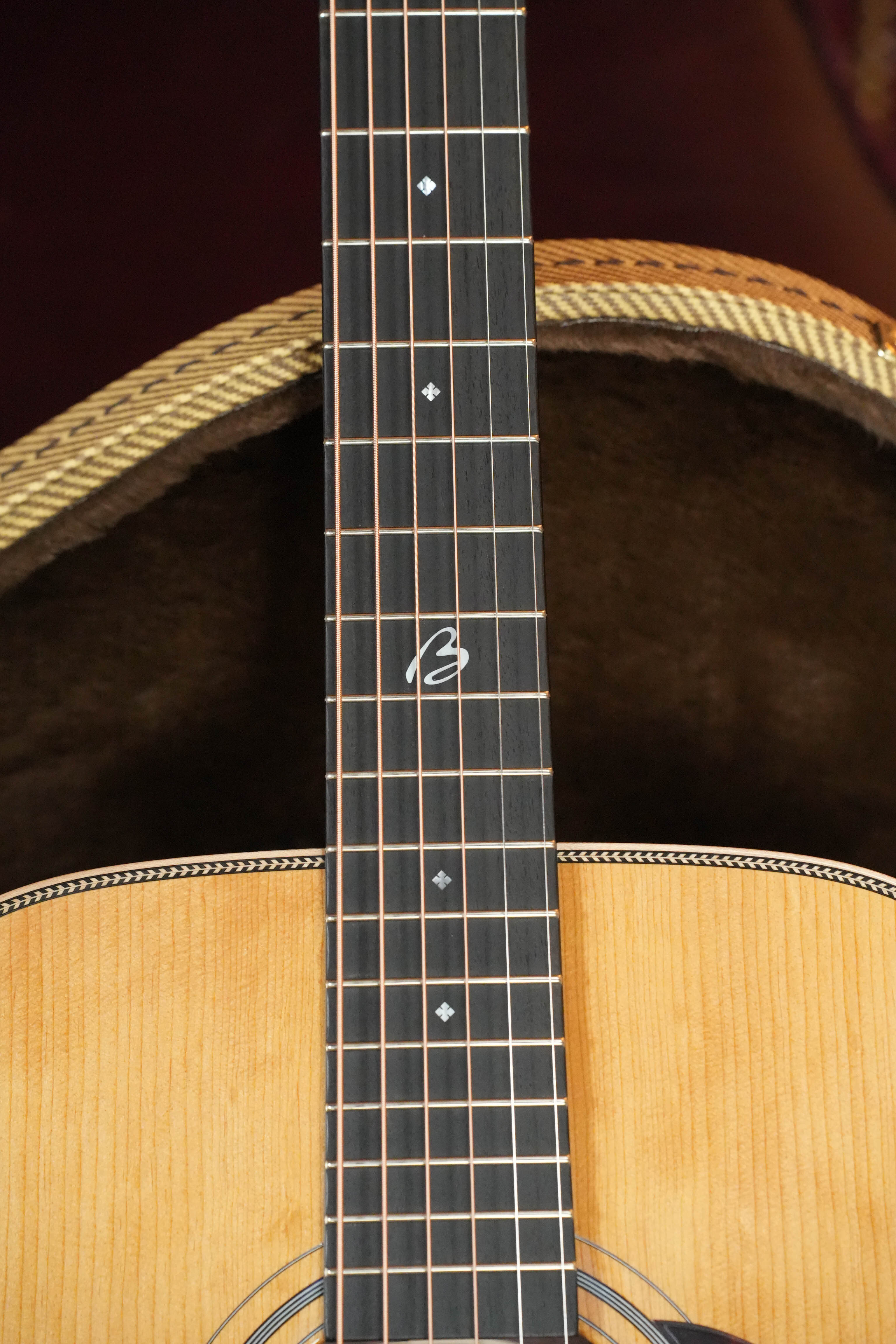 Close-up of the *New 2026 Model* Boucher BG-52-G Torrefied Adirondack/Rosewood Bluegrass Goose Gold Pack Dreadnought Acoustic Guitar #1421 by Boucher Guitars, showing diamond inlays, stylized “E,” light wood body, and a hardshell case behind.