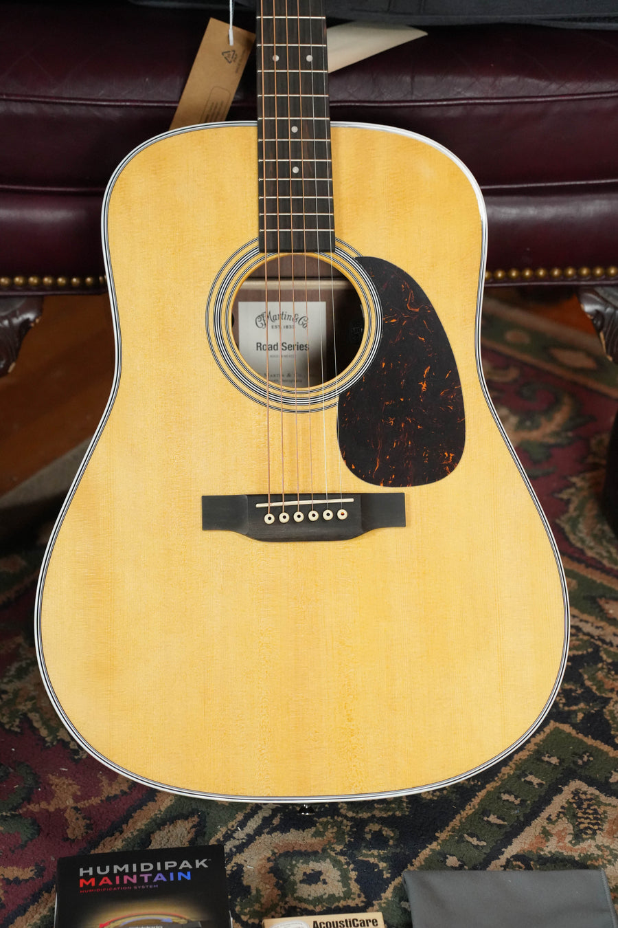 A close-up of a *New 2026 Model* Martin D-13E Retro Road Series Dreadnought Guitar by Martin & Co., featuring a light wood finish, black pickguard, six strings, product tag on the headstock, and a Humidipak Maintain package below.
