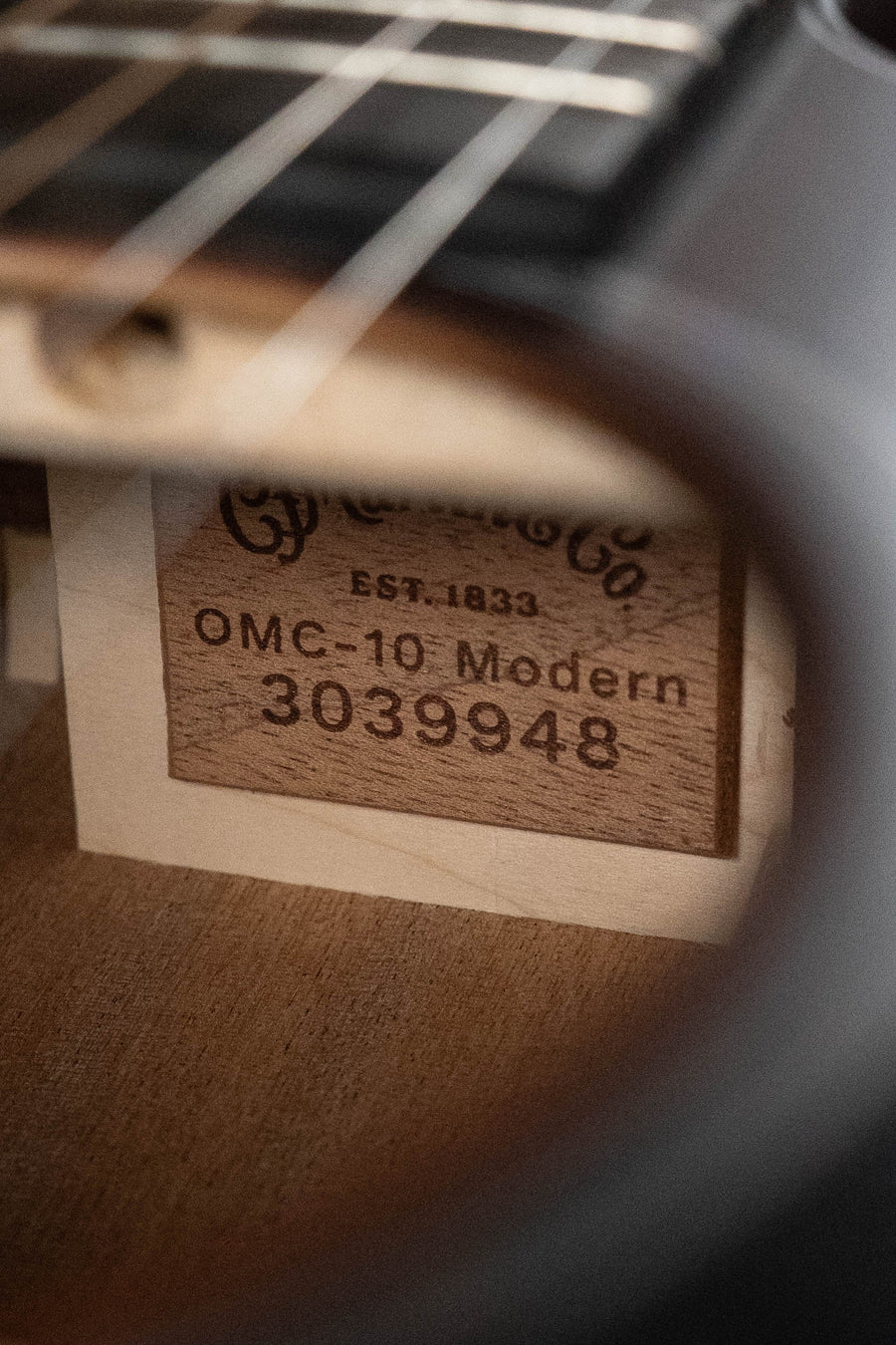 Close-up of the *New 2026 Model* Martin & Co. OMC-10E Modern Burst interior label (#9948) viewed through the sound hole and under the strings on this Road Series spruce/sapele cutaway guitar with scalloped X bracing.