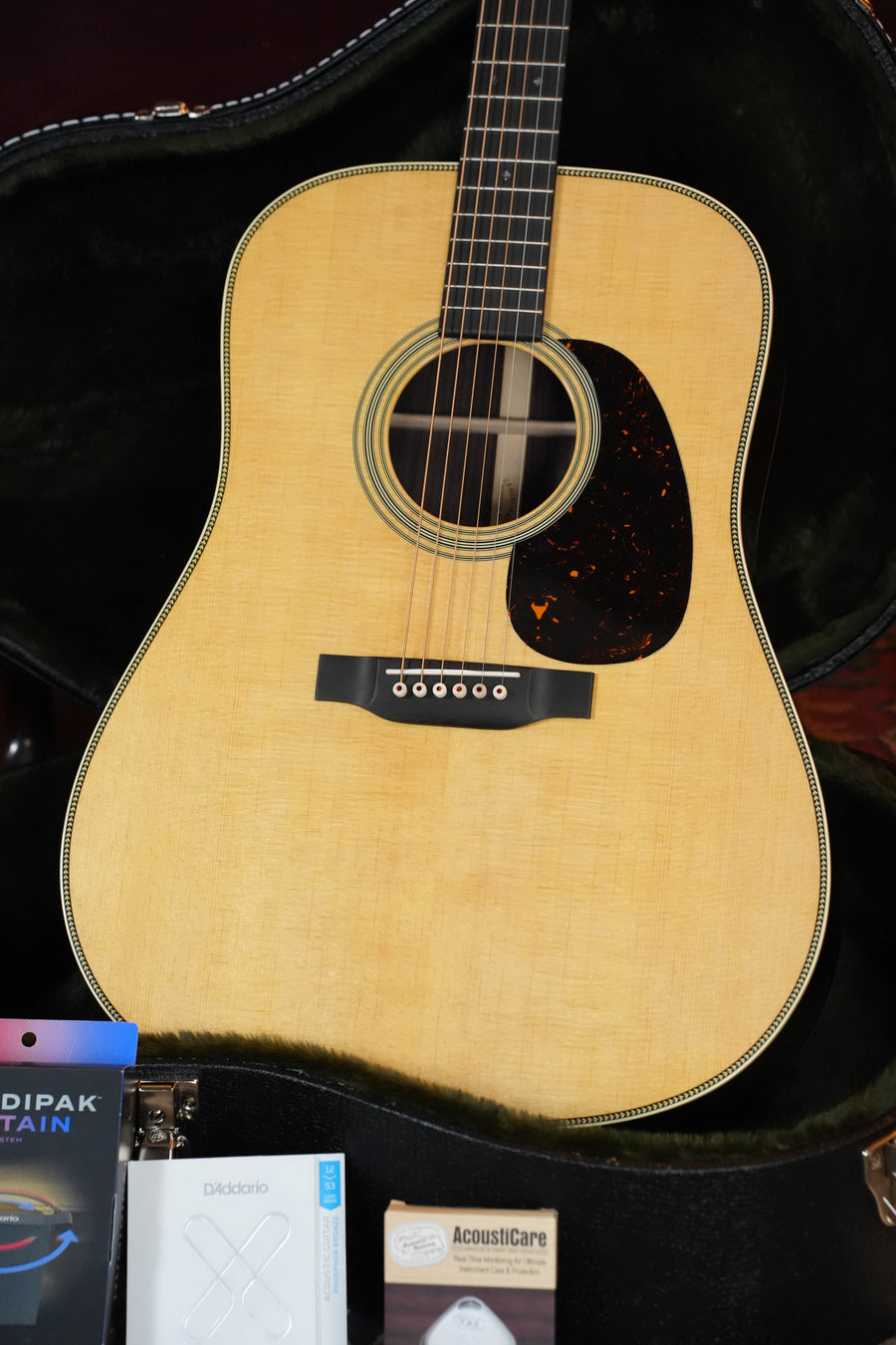 A close-up of the Martin & Co. *New 2026 Model* Super HD-28 Spruce/Indian Rosewood Dreadnought Acoustic Guitar #5773 in its case, with guitar string packs and an AcoustiCare polish kit in front.