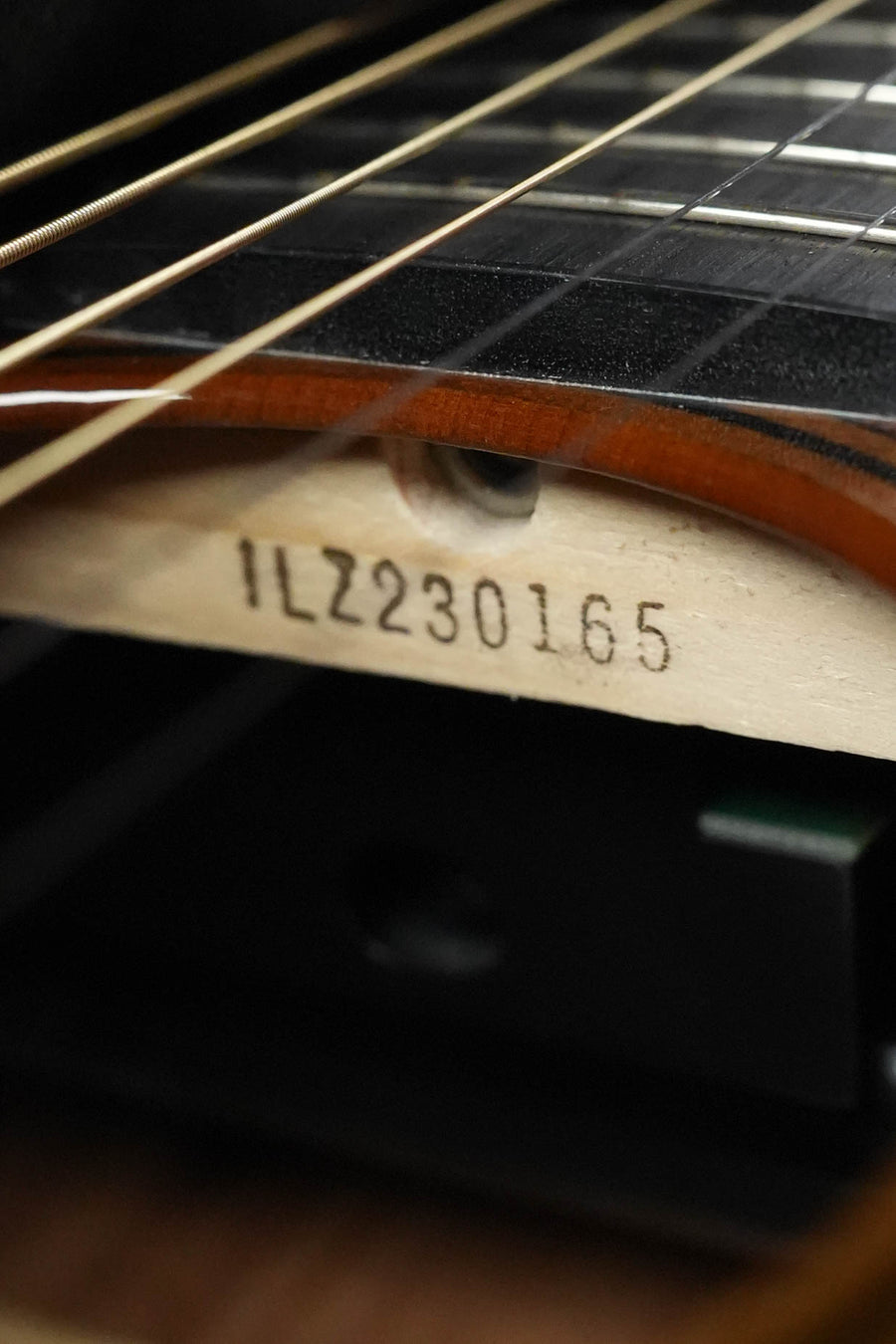 Close-up of a Yamaha TAS3C-SBD Sandburst Concert Guitar (#0165) soundhole, showing the serial number stamped on the Sitka spruce top bracing. Strings and part of the fretboard are visible above.