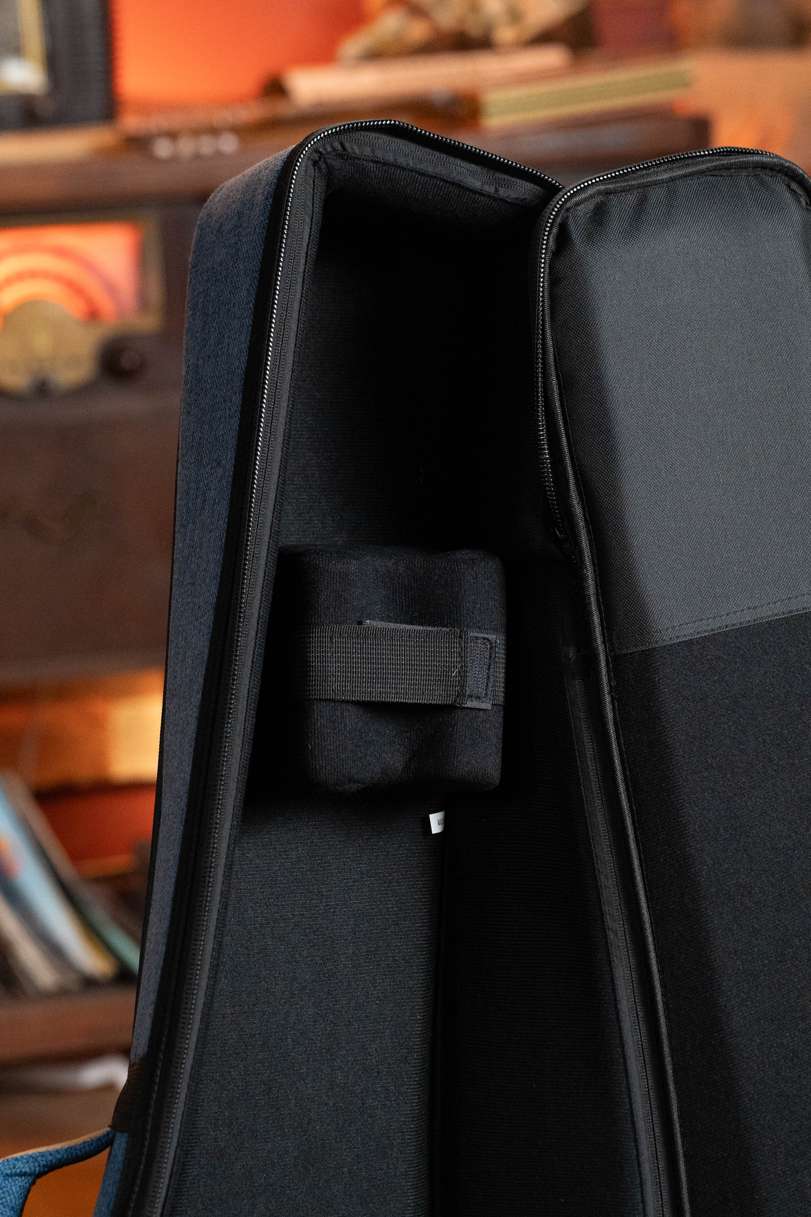 A close-up shows the interior of the Ortega OSOCABJ-OC Banjo Soft Case in Ocean Blue, with black padded lining and a small Velcro strap. Blurred ocean blue records and wooden furniture appear in the background.