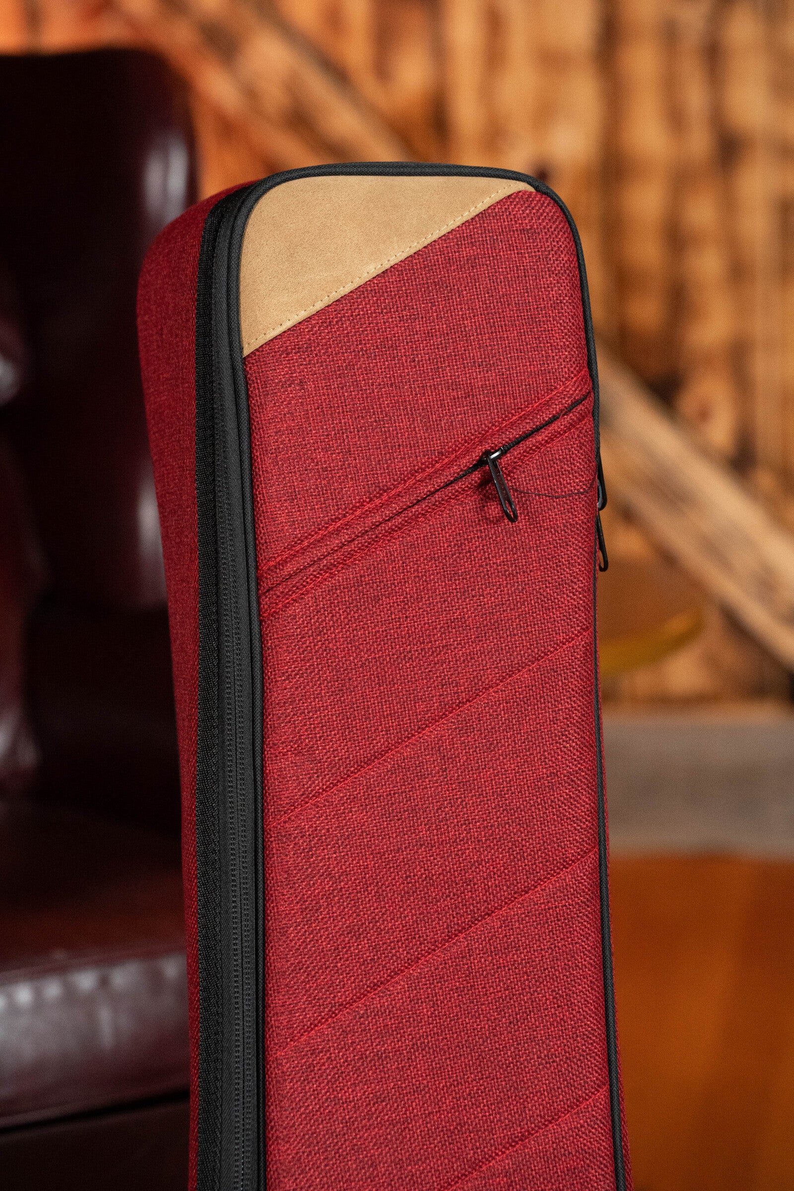Close-up of the Ortega OSOCABJ-BX Banjo Soft Case in Bordeaux Wine, featuring a black zipper and tan accent on top, set against a blurred indoor background with wood and leather elements.