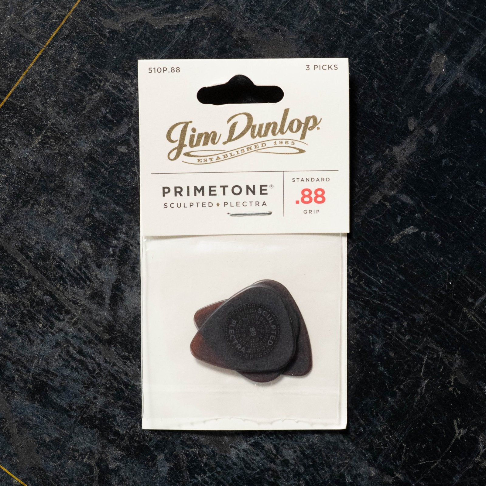 A Dunlop Primetone Standard Grip Pick 3 Pack (510P) in a clear pouch, labeled .88 gauge, sits on a dark textured surface.
