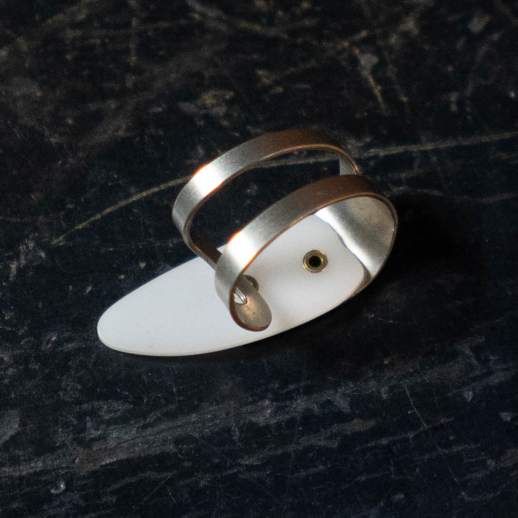 The ProPik Metal/Plastic Thumb Pick Large (11-206-3002) by ProPik features two parallel bands with a white oval accent and a non-slip design, including a small central hole for added style and comfort. Displayed on a dark, textured surface.