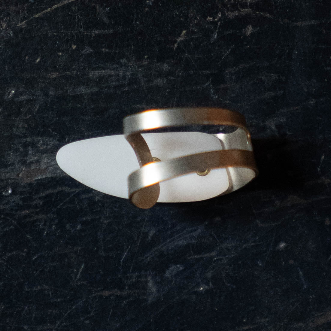 A ProPik Metal/Plastic Thumb Pick Large (11-206-3002) by ProPik, featuring a silver and white non-slip design, rests on a dark, textured surface.