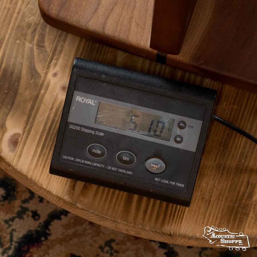 A digital shipping scale on a wooden table displays 5.10 pounds—the perfect weight for the Squirrel Hunter Ornate Rosewood Dreadnought by Squirrel Hunter. A patterned rug is partially visible in the background.