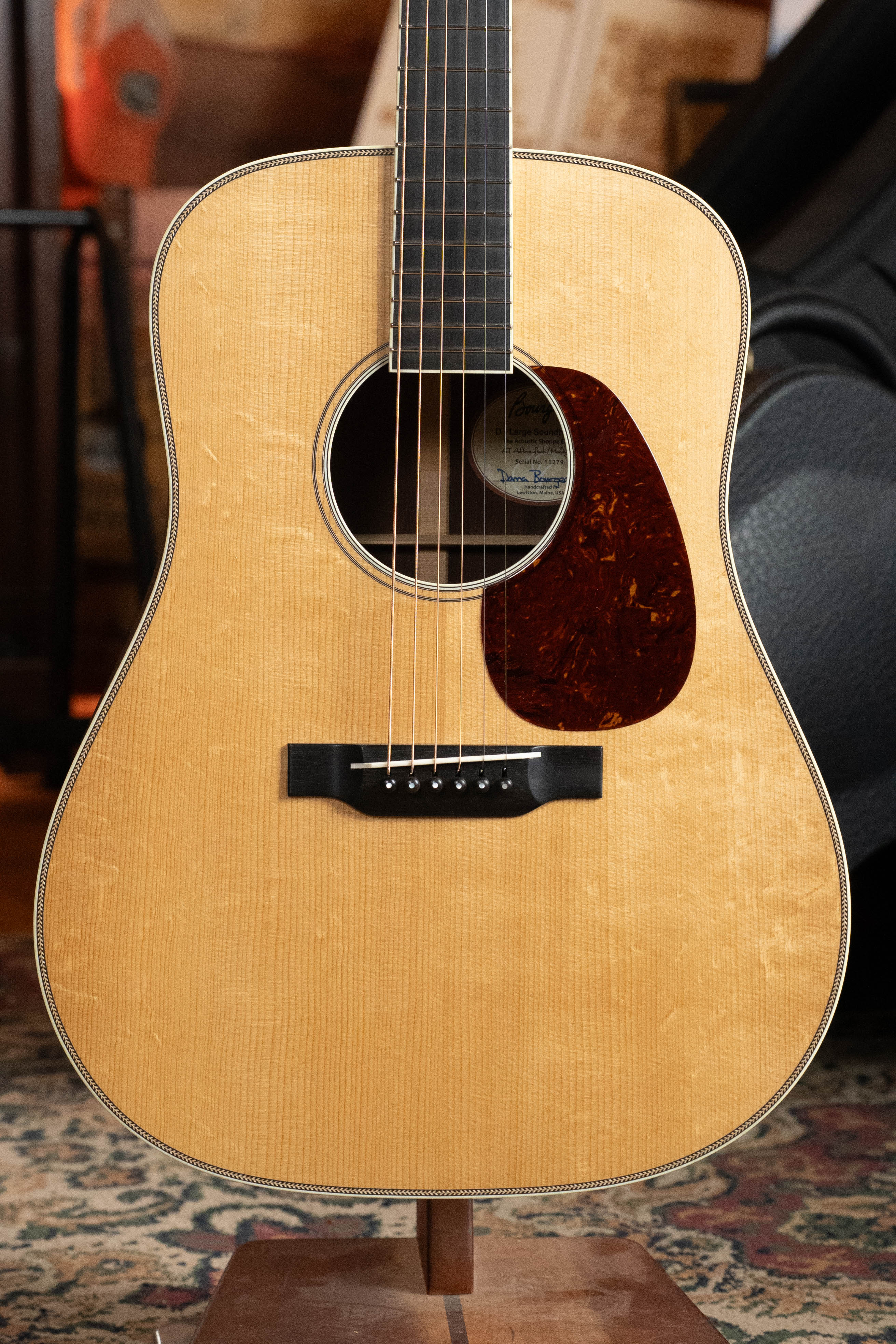 A close-up of the Bourgeois TAS LSH Professional Series Satin Dreadnought Guitar with light wood finish and dark pickguard, upright on a stand. Pre-order 25% deposit only from Bourgeois.