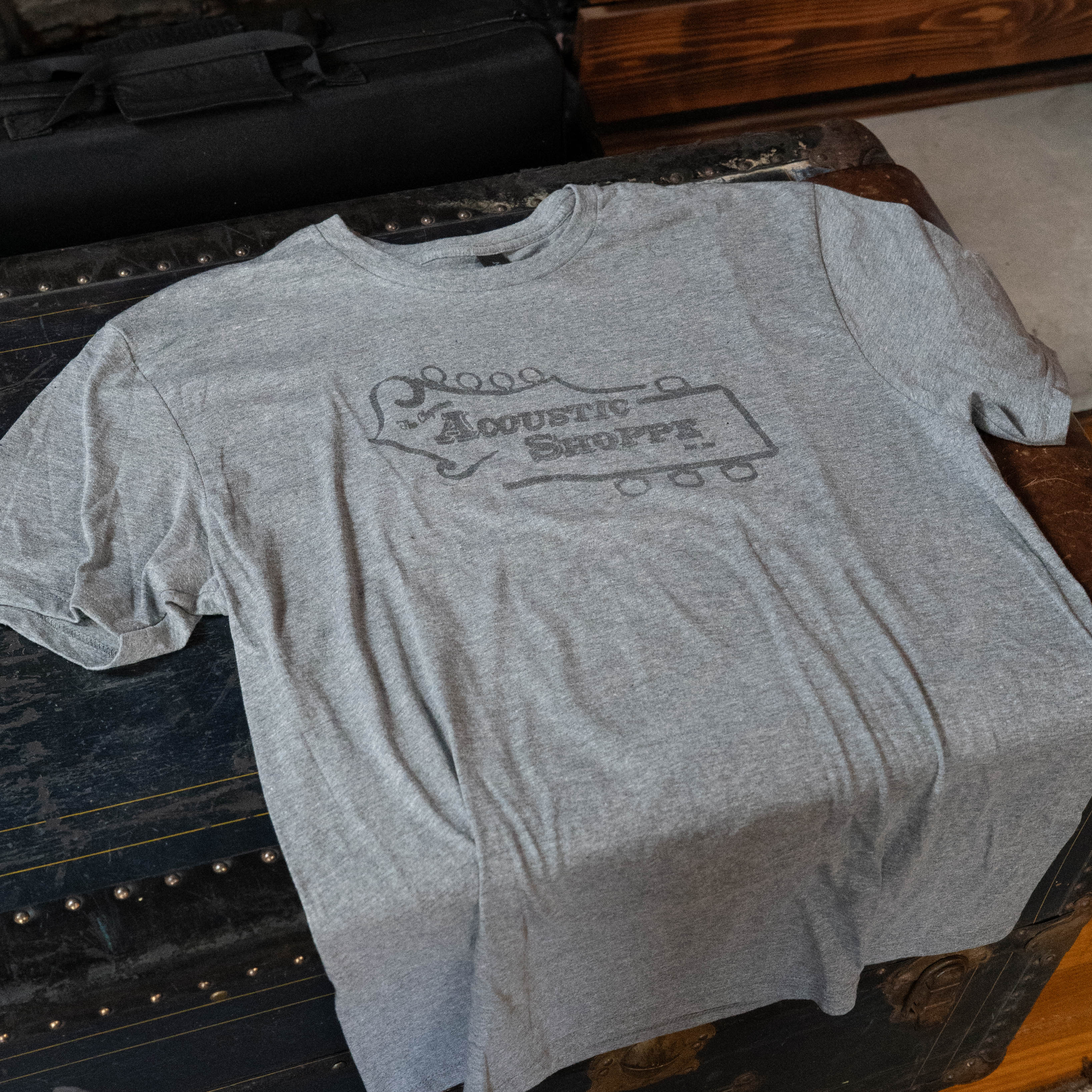 The TAS Logo Tone-On-Tone Shirt by Amplify Screen Printing & Promotions features a light gray design with a guitar headstock and Acoustic Shoppe print—perfect for music lovers seeking stylish comfort.