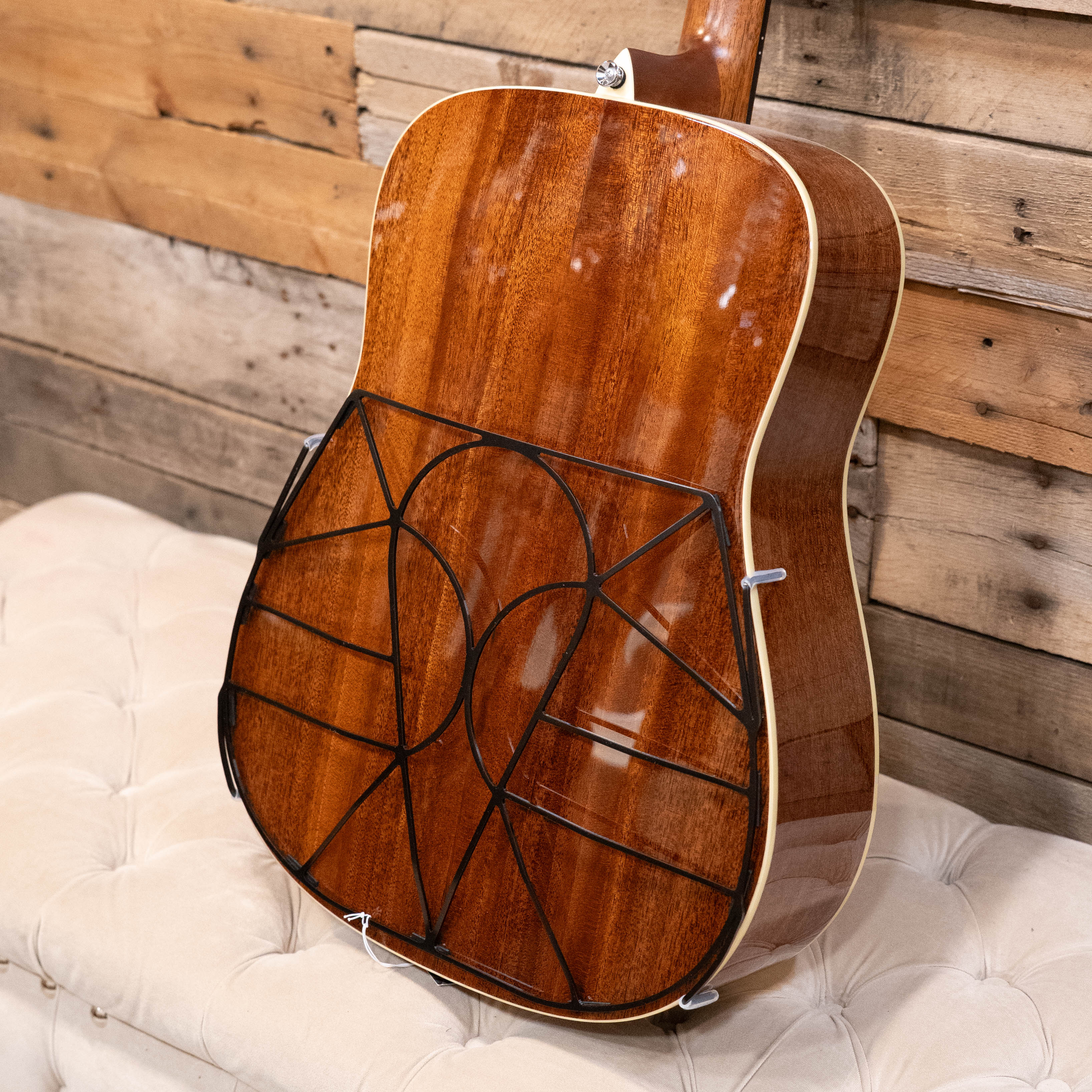 A Tone-Gard Dreadnaught Guitar D-Gard by Tone-Gard sits on a cushioned bench, its polished back fitted with a black wireframe protector, evoking mandolin-style designs. Rustic wooden planks serve as the backdrop.