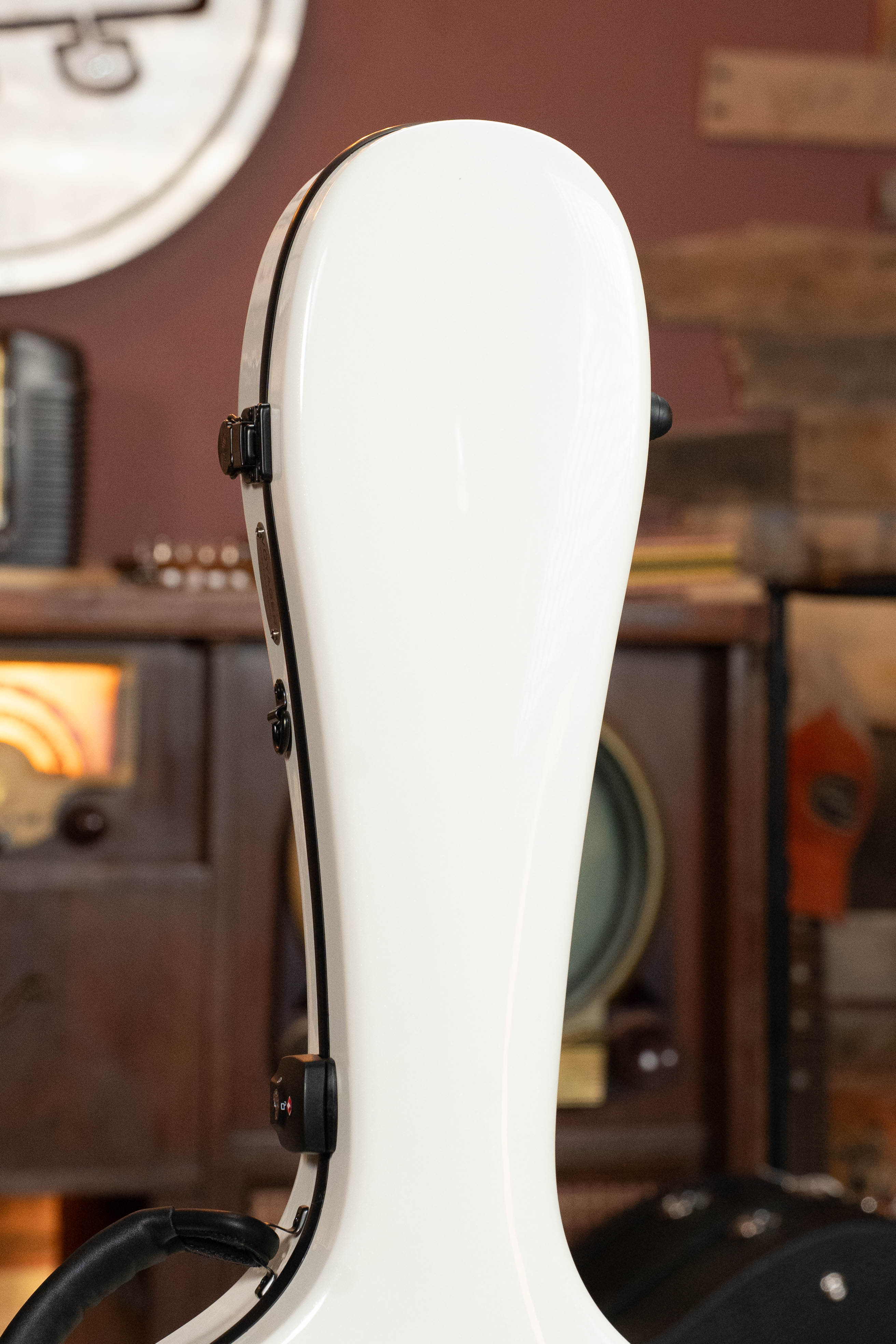 The TKL Voyager Universal Pearl Glacier/Blue Carbon Fiber Dreadnought Case stands upright indoors, its white lightweight design with black clasps set against vintage wooden furniture and musical instruments.